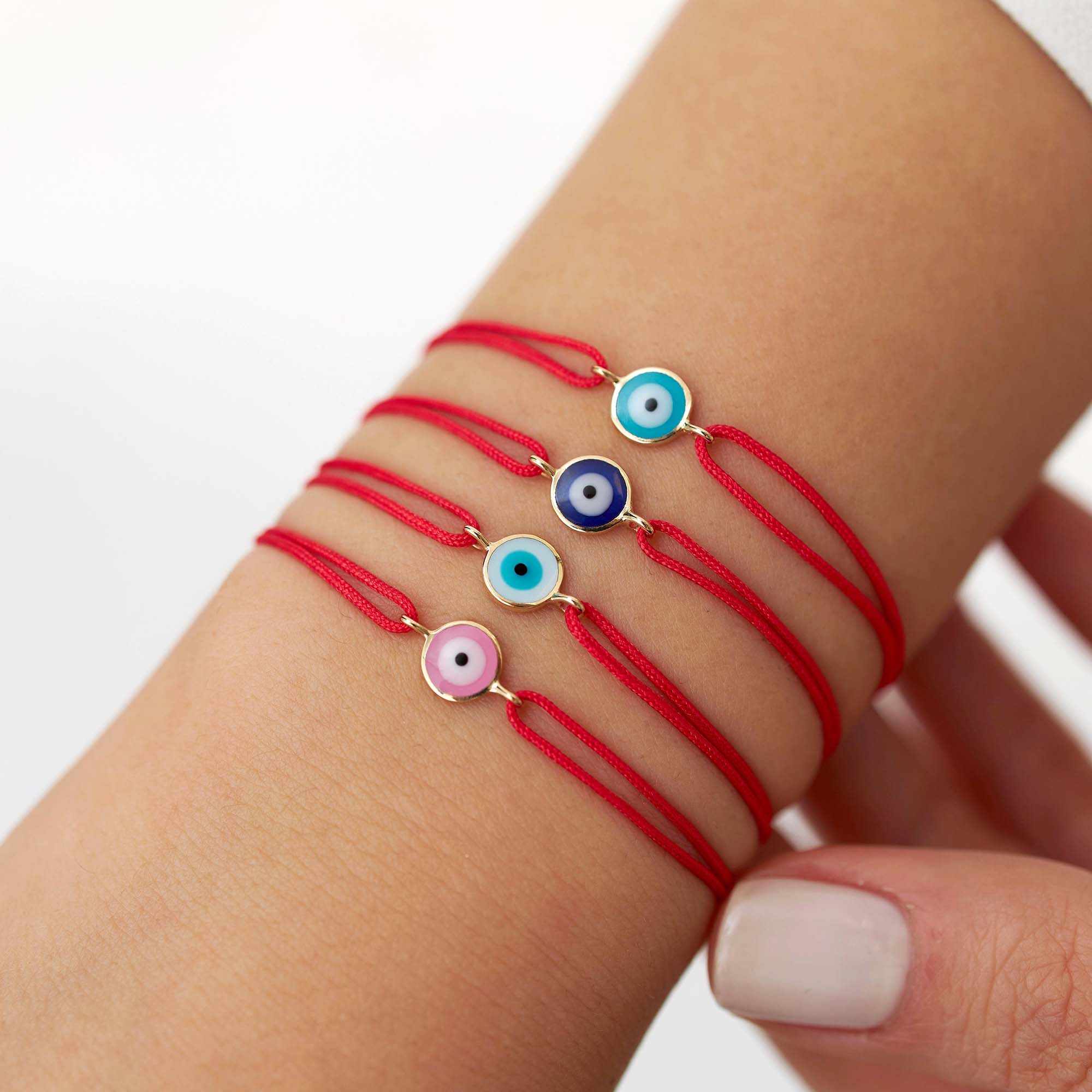 Red string bracelets with colorful evil eye charms on a wrist against a white background