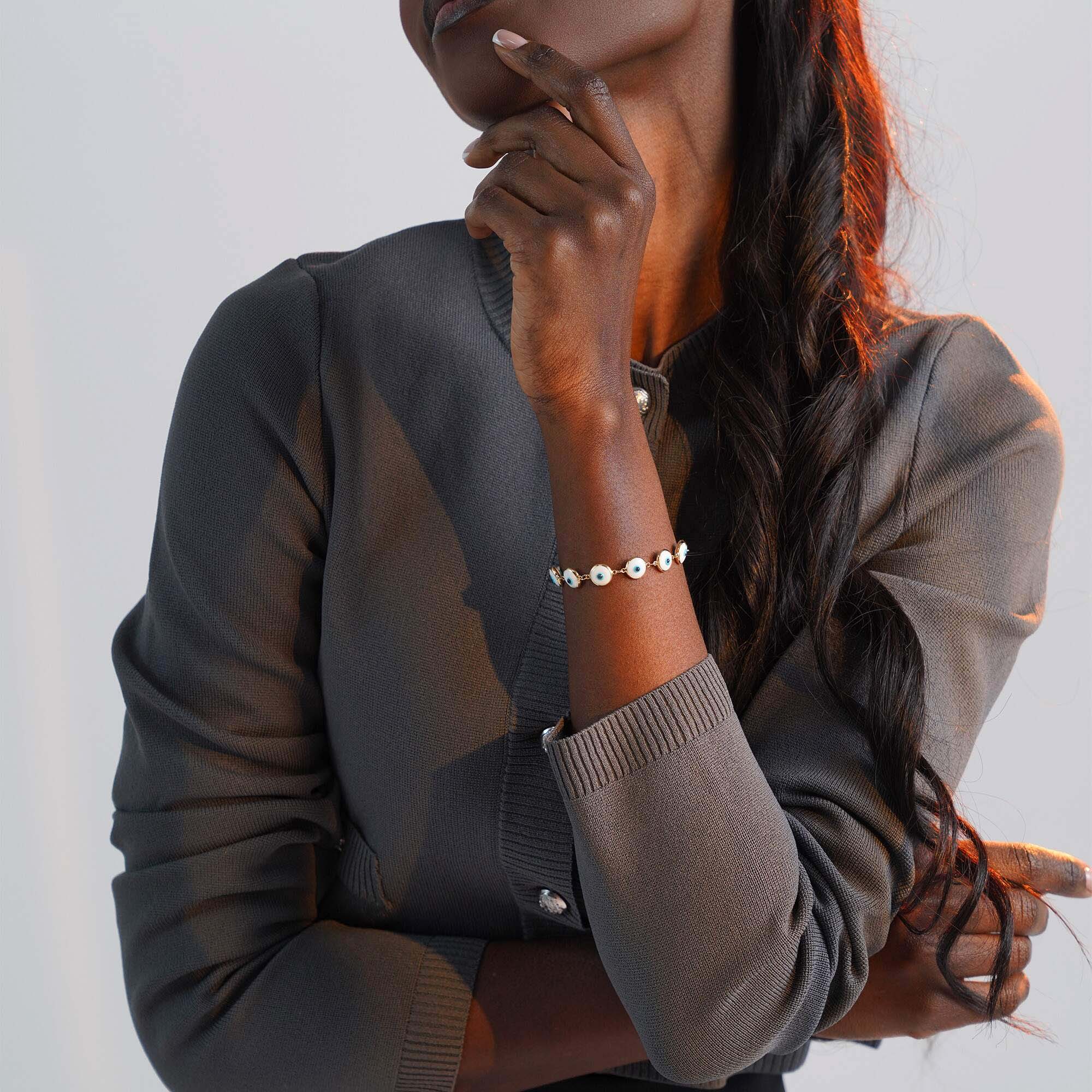 Person wearing a bracelet with white evil eye charms on a plain background