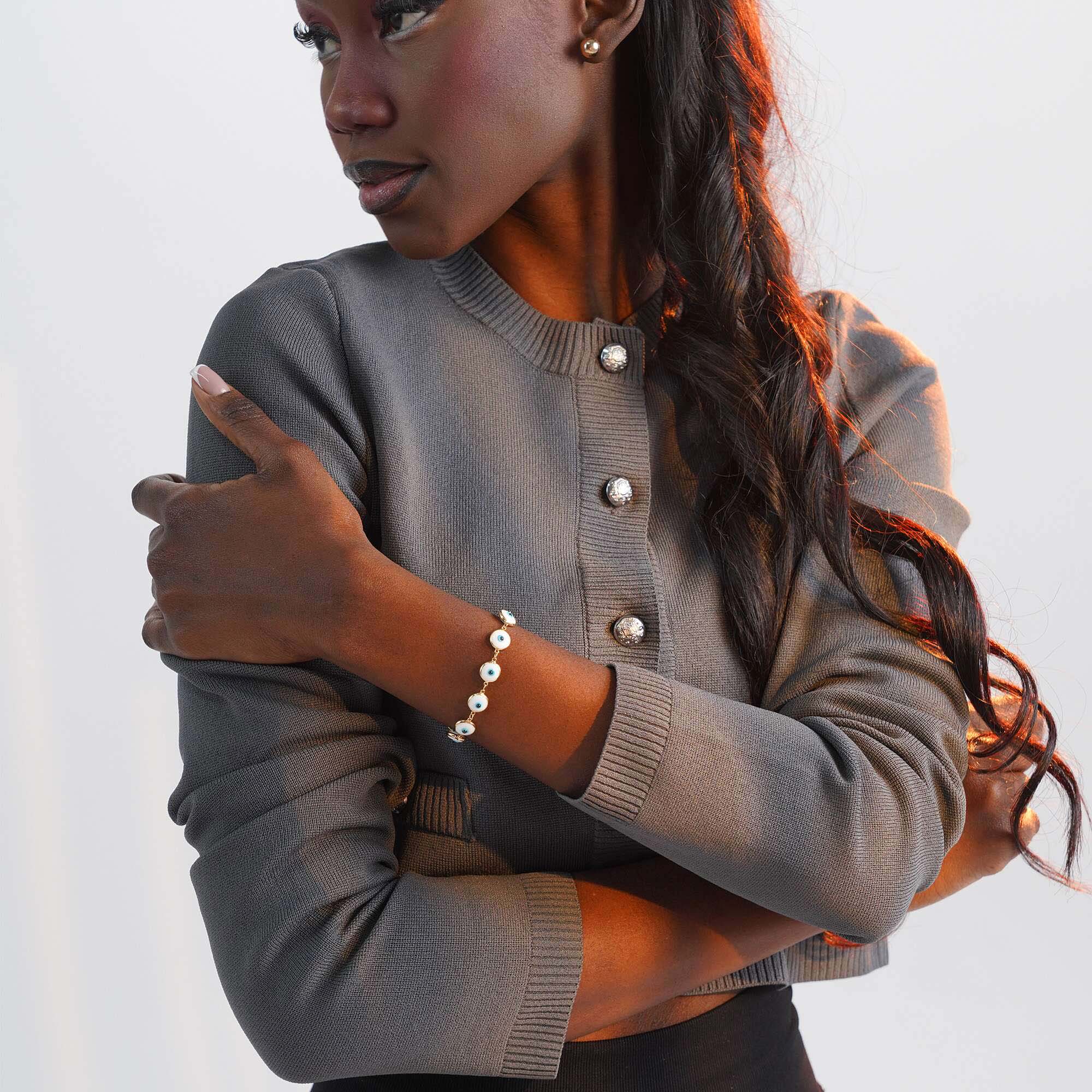 Person wearing a bracelet with white evil eye charms on a plain background
