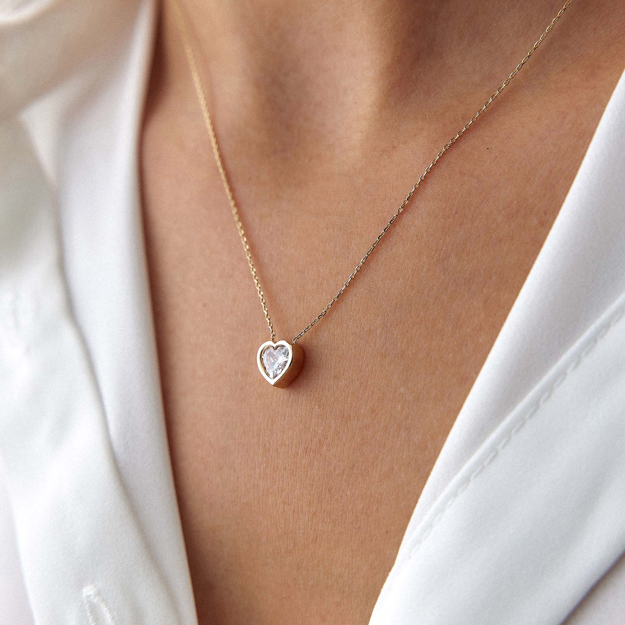 Gold necklace with a heart-shaped pendant worn by a person in a white outfit.