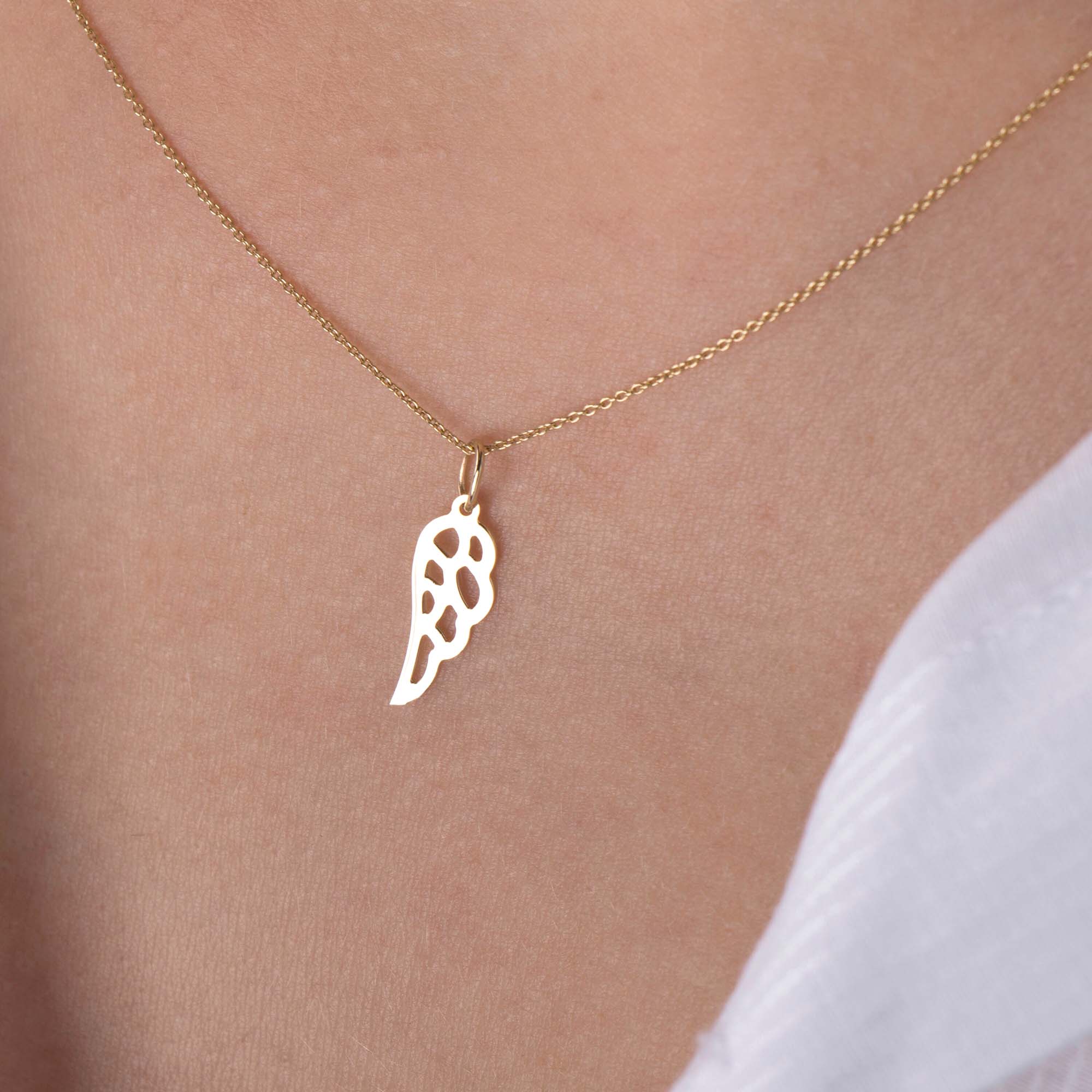 An up-close image of a minimal angel wing pendant necklace worn by a model.