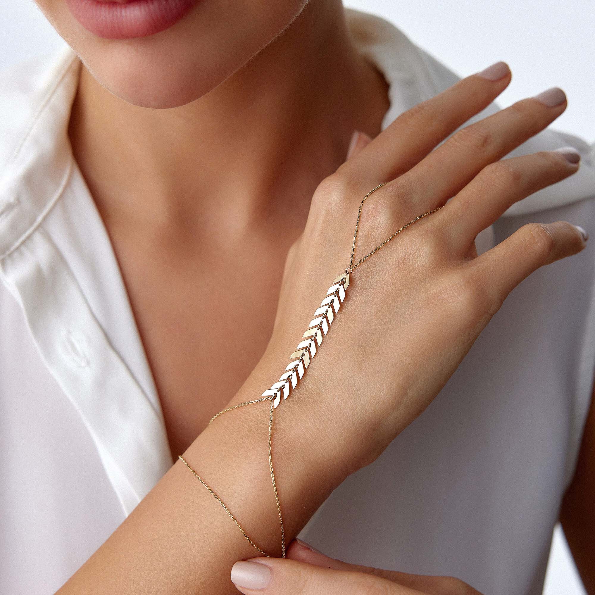 Hand wearing a delicate gold hand chain bracelet with small beads on a white background