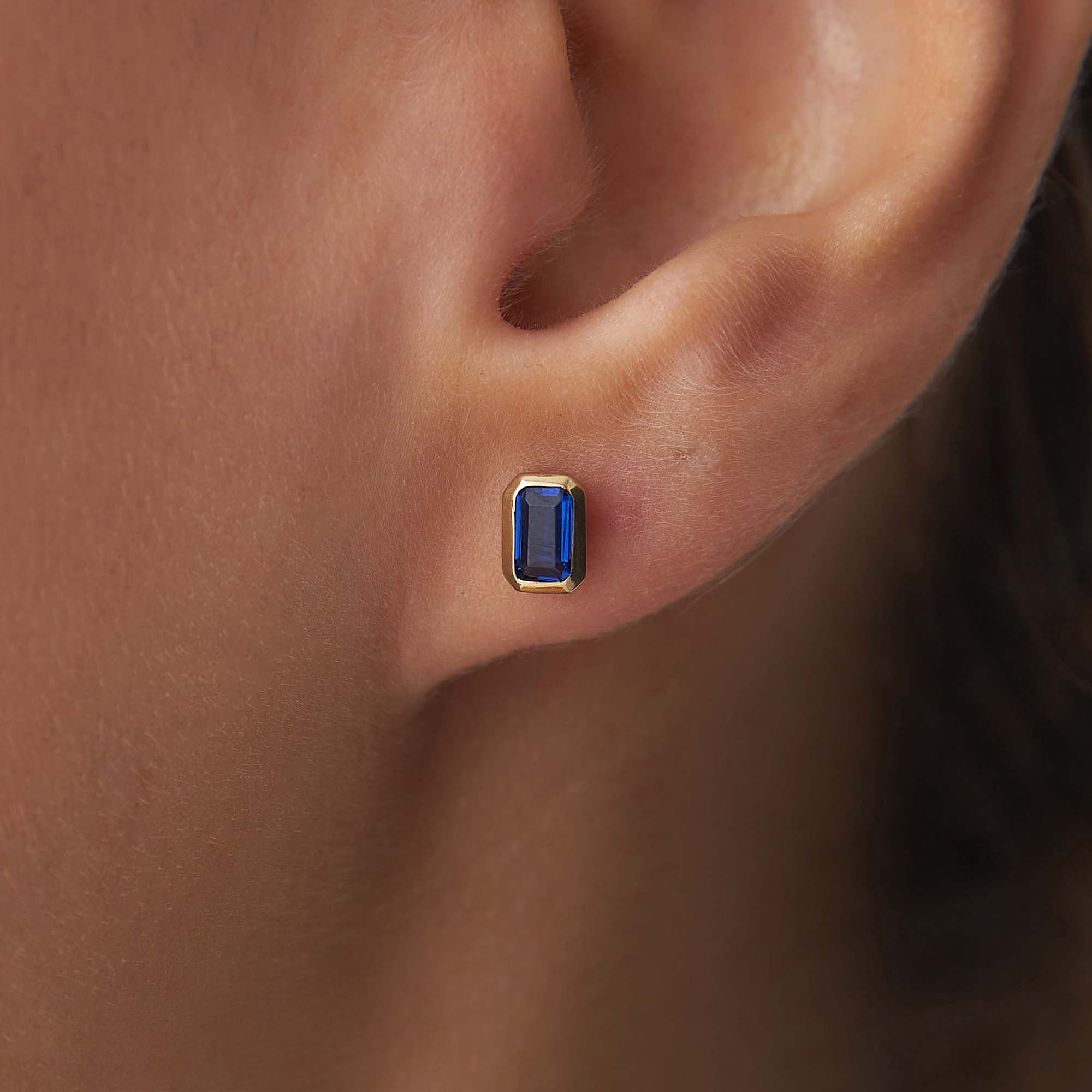 Gold earring with a blue gemstone worn on an ear