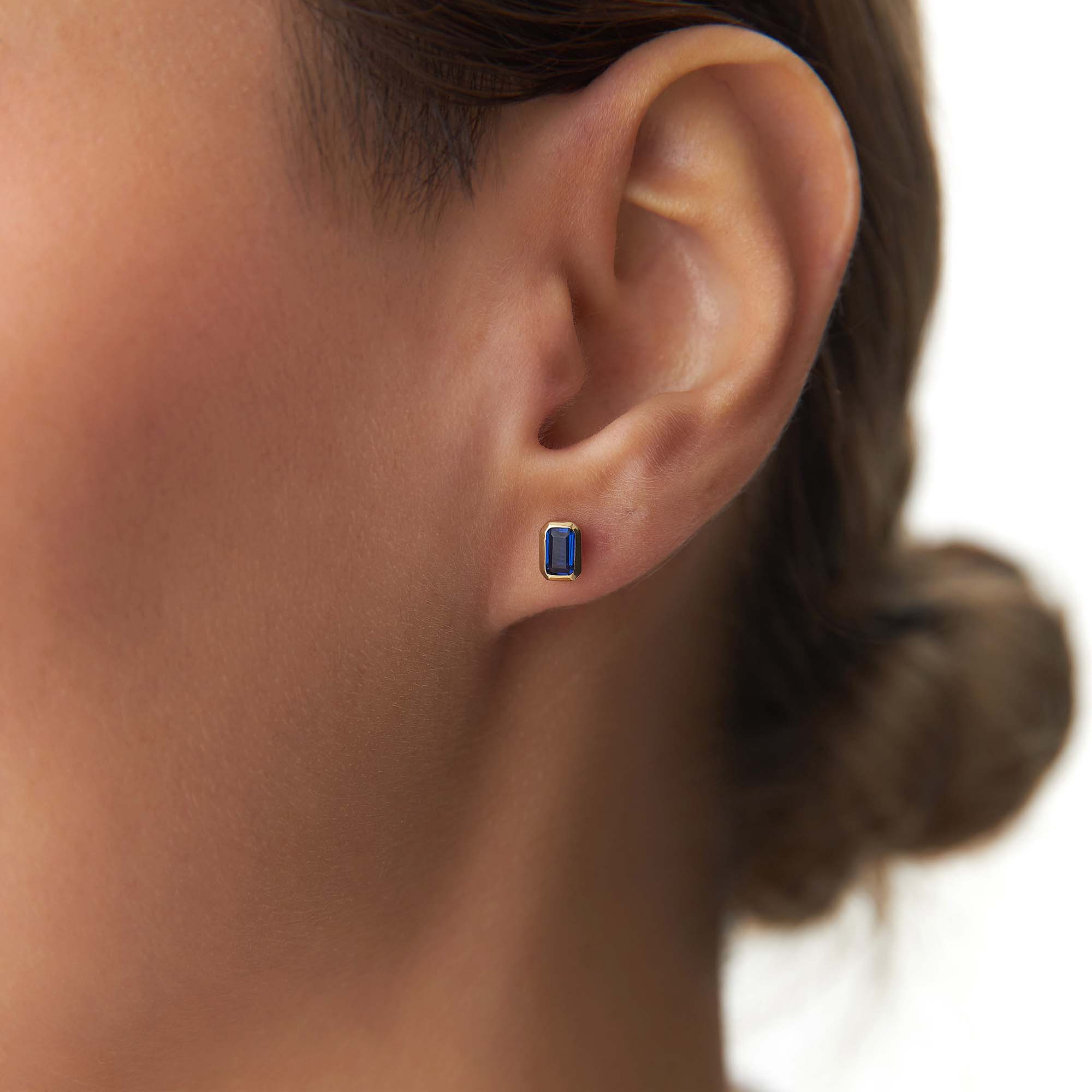Close-up of an ear wearing a blue gemstone stud earring with a blurred background