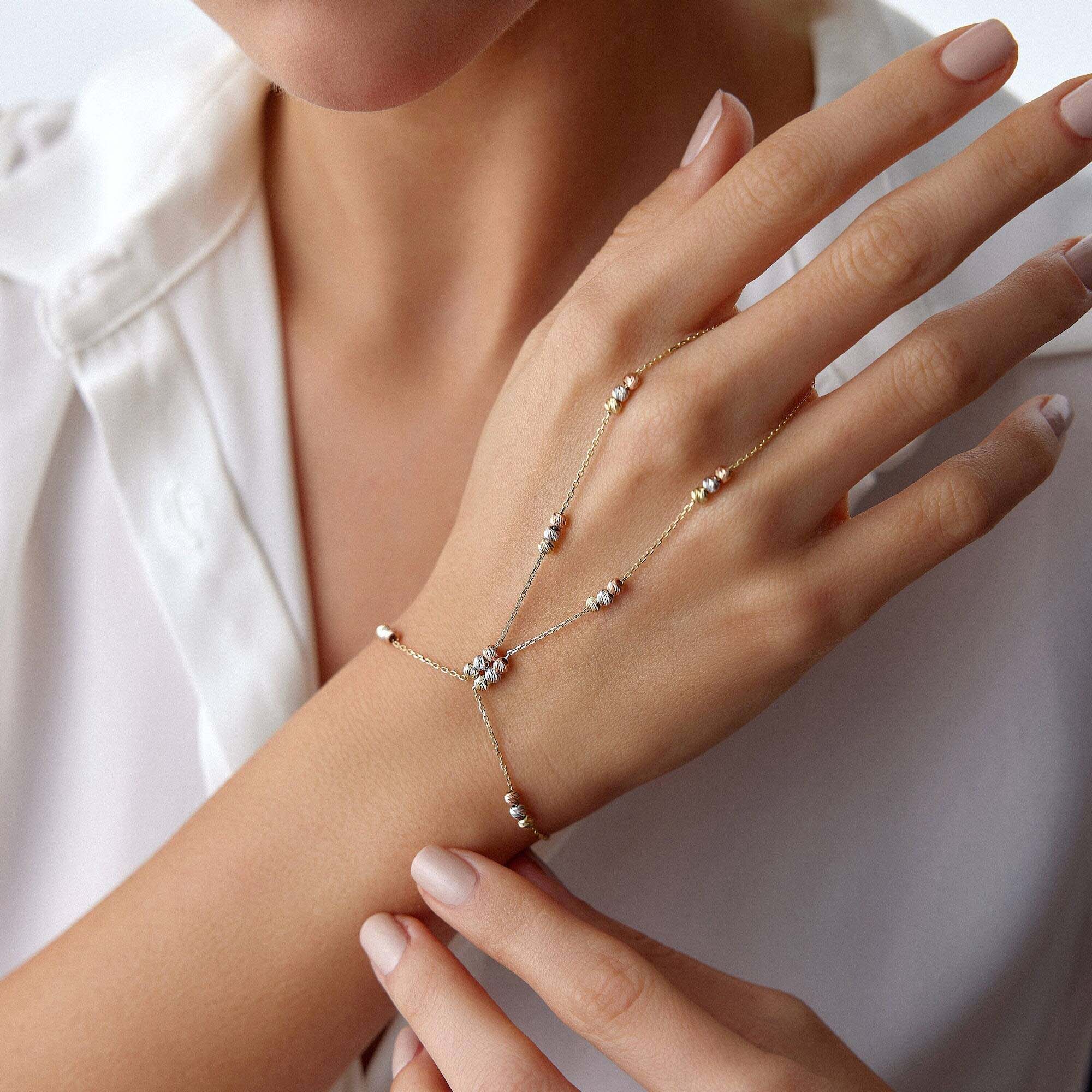 Hand wearing a delicate gold hand chain bracelet with small beads on a white background
