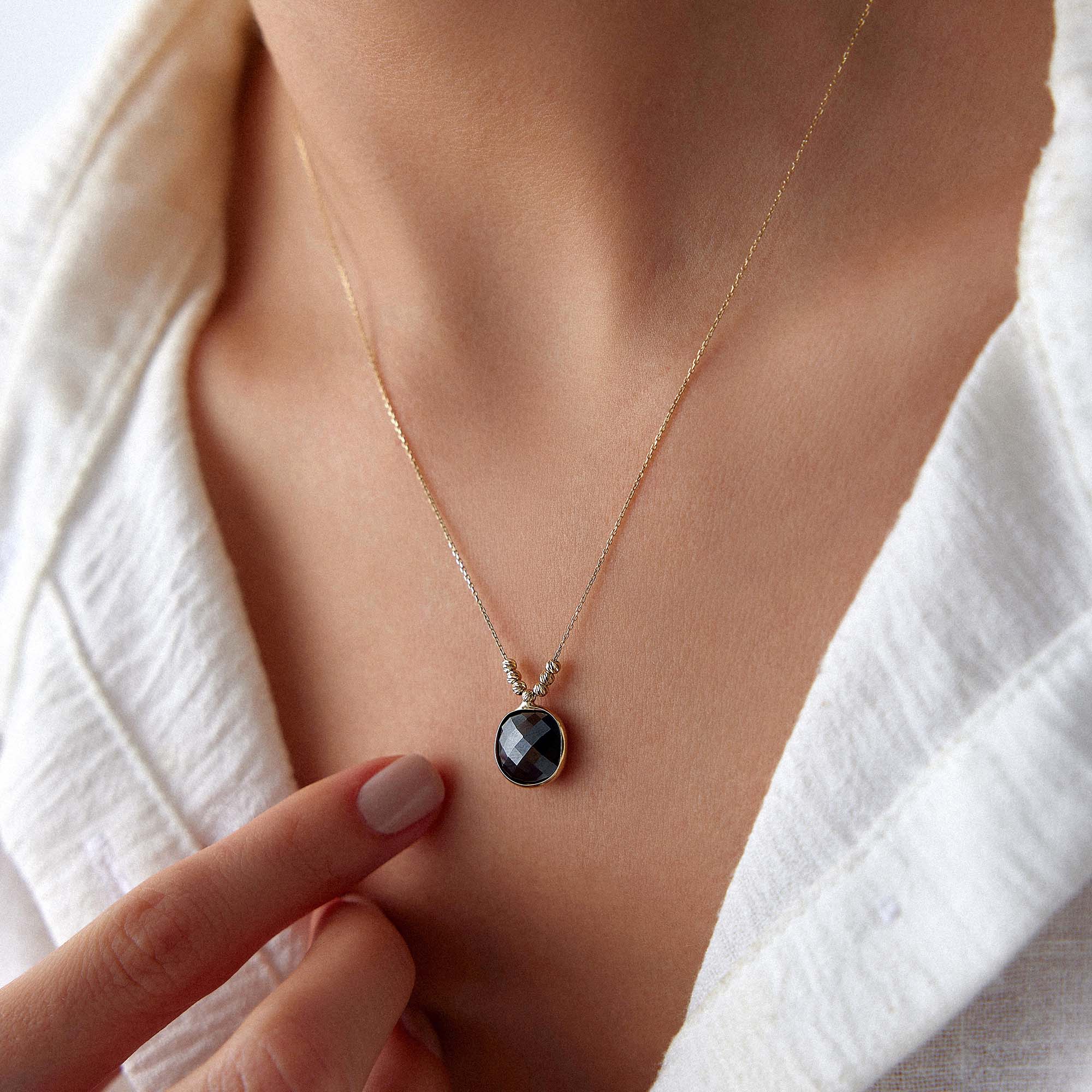 Necklace with a black crystal pendant worn by a person in a white outfit