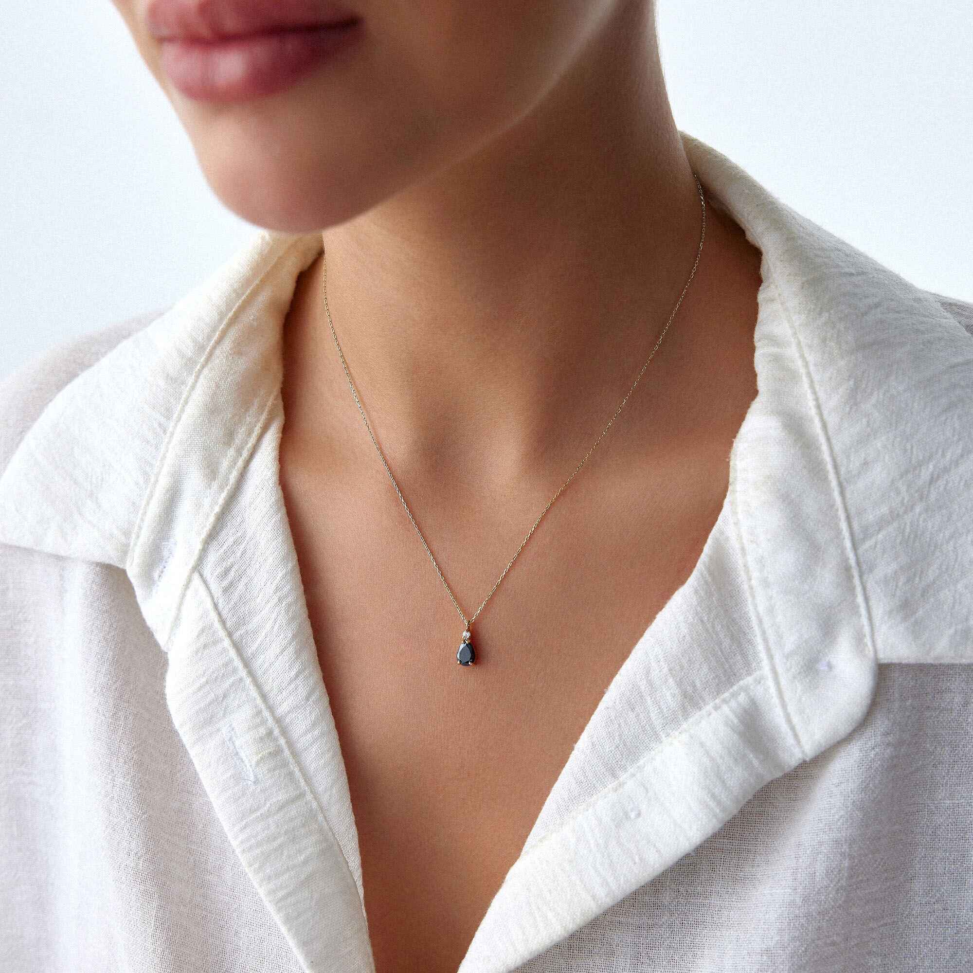 A close-up image of a model wearing a black drop necklace