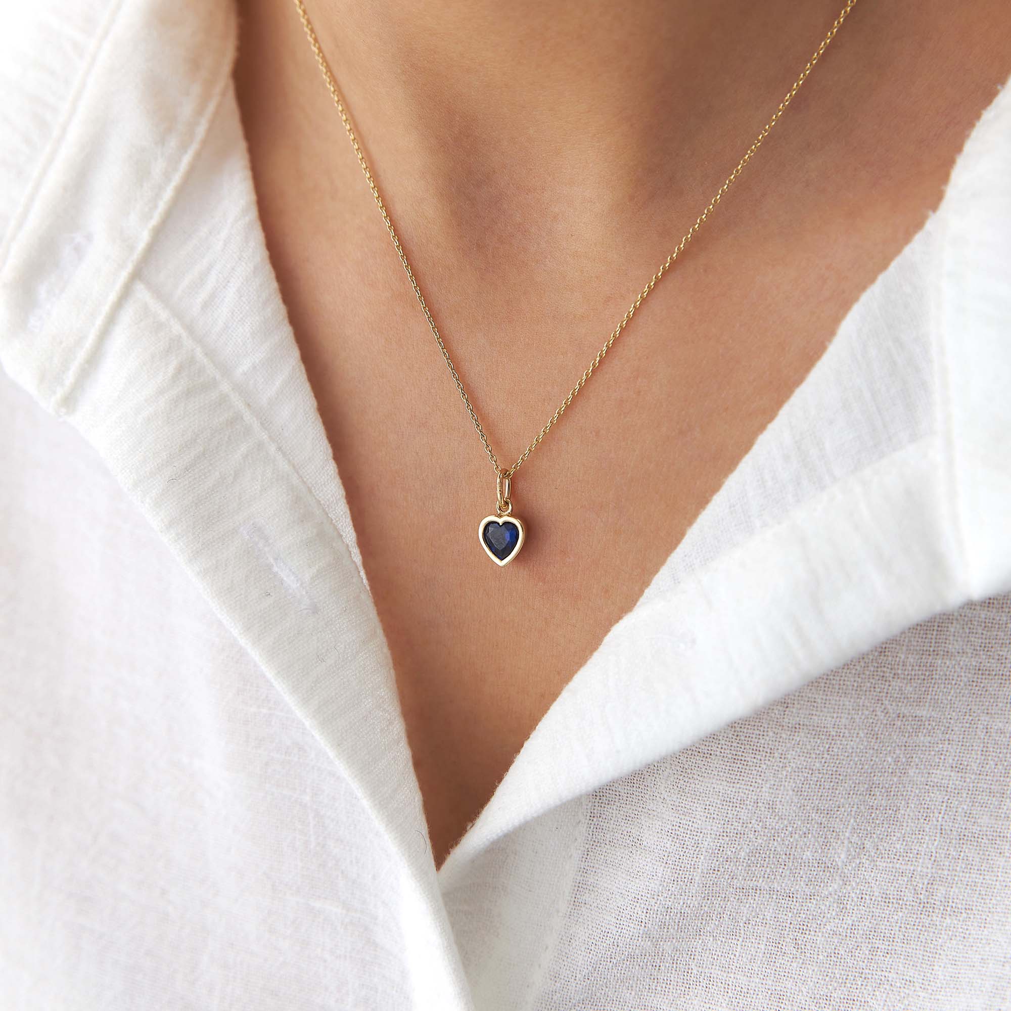 Gold necklace with a heart-shaped blue gemstone pendant worn by a person.