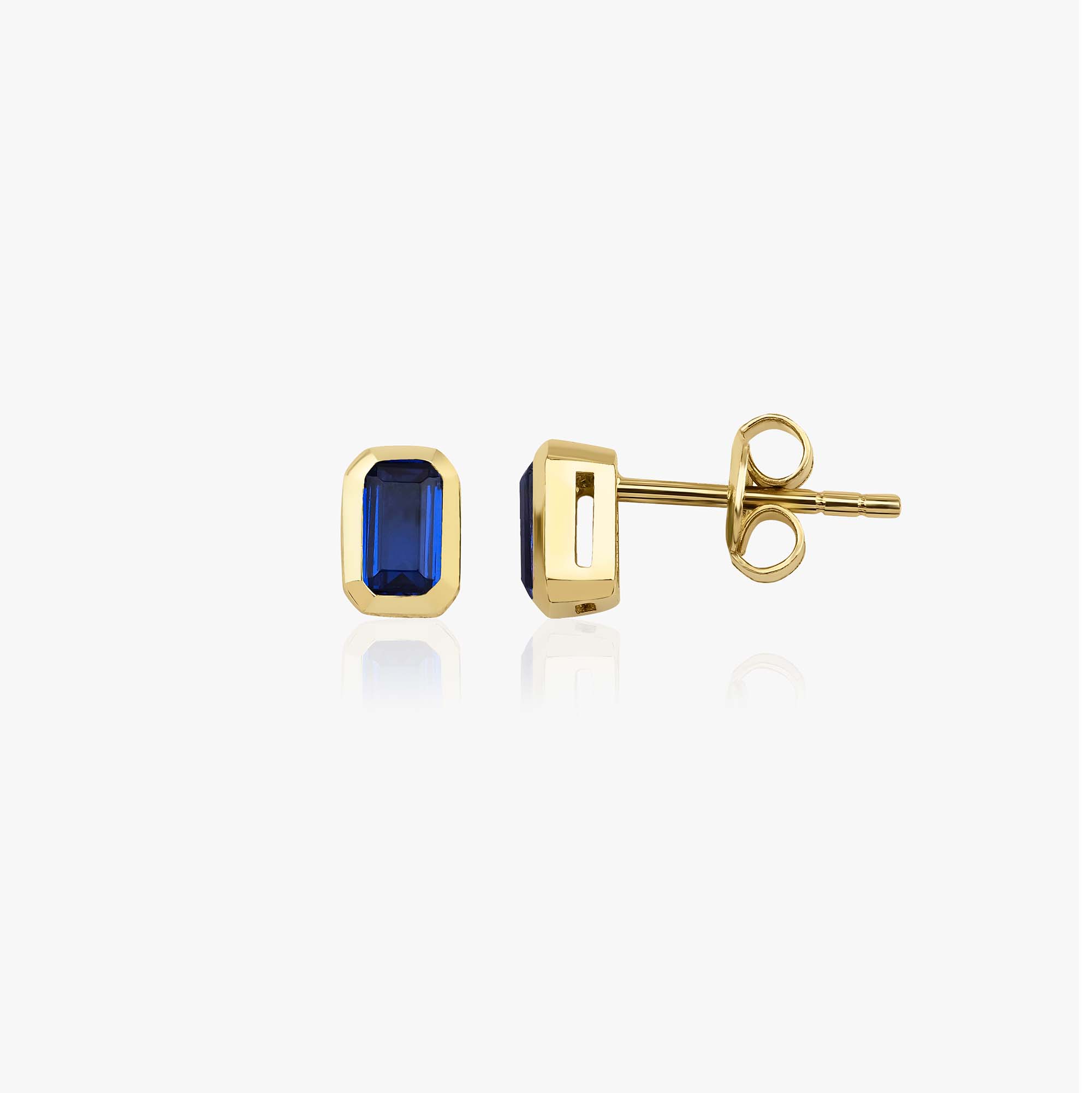 Gold earrings with blue gemstones on a white background, one shown sideways