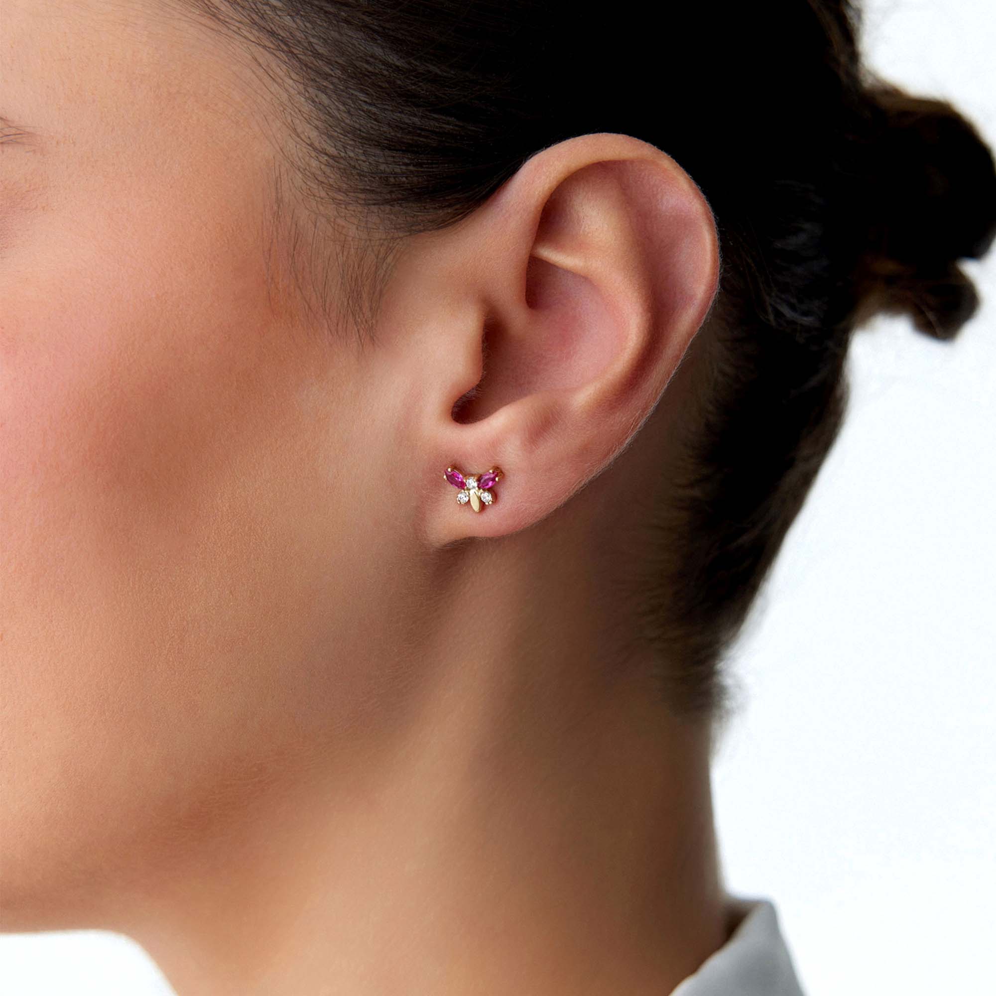 Close-up of an ear wearing a colorful butterfly stud with a blurred background