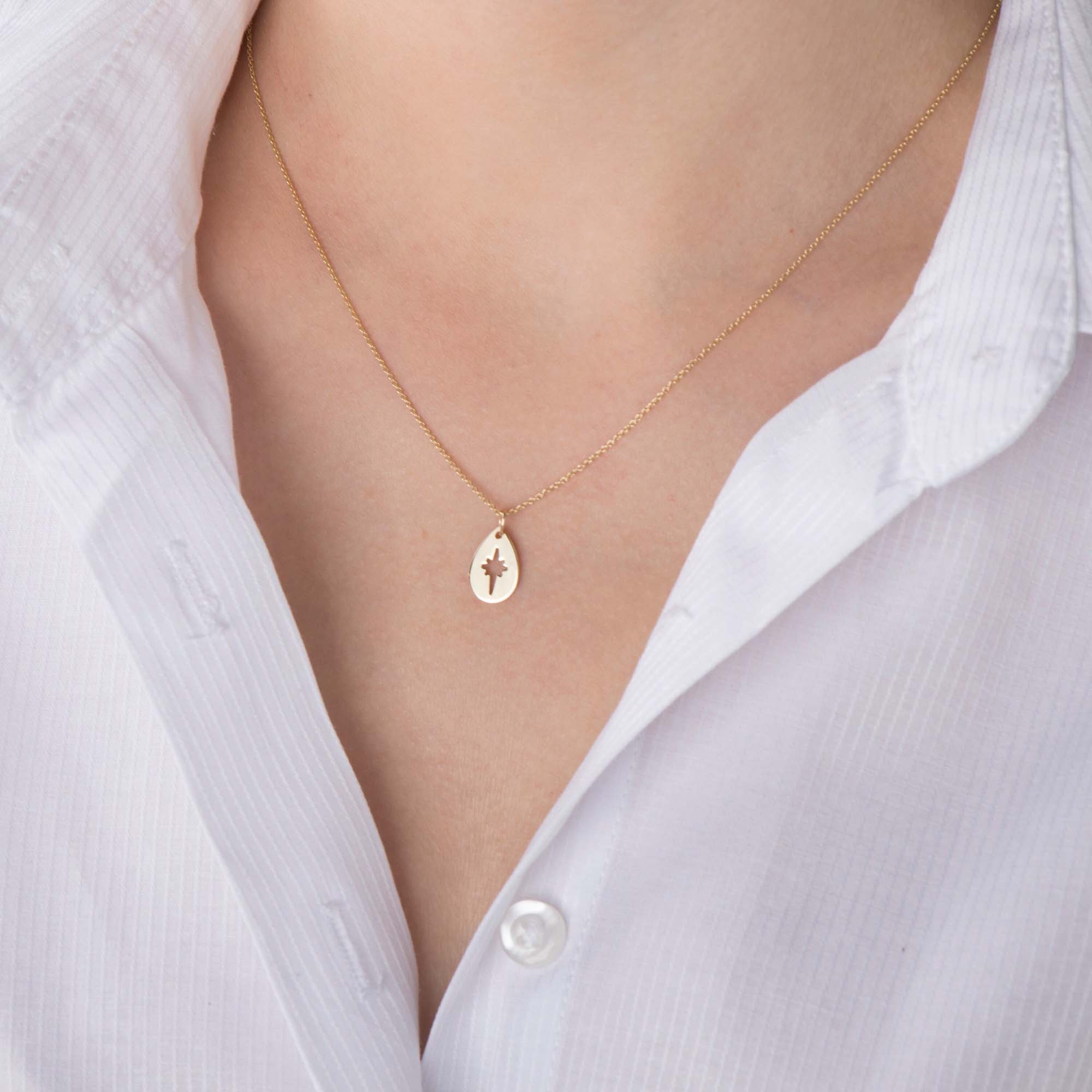 A 14k yellow gold necklace with a raindrop-shaped pendant on a person wearing a white shirt.