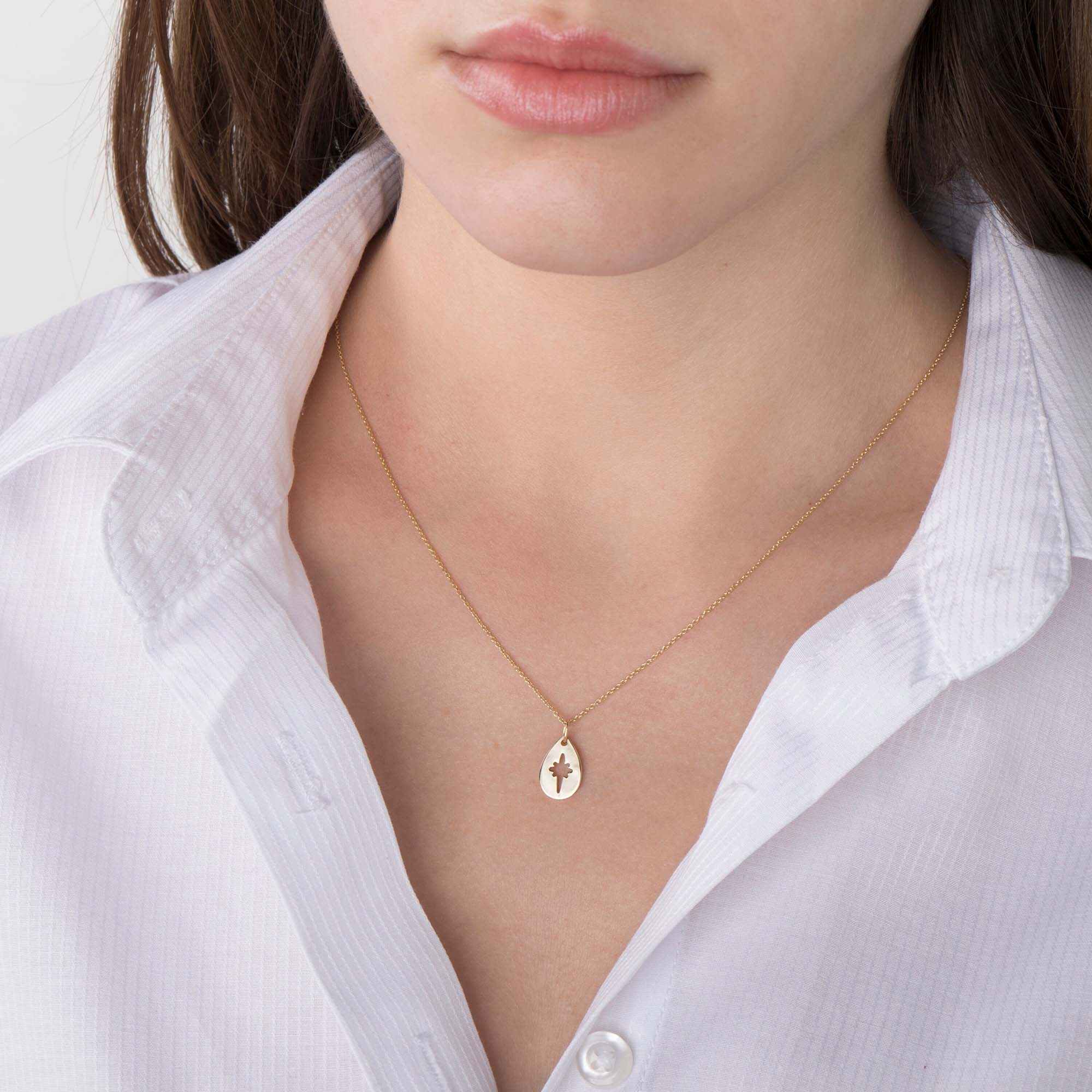 A 14k yellow gold necklace with a raindrop-shaped pendant on a person wearing a white shirt.