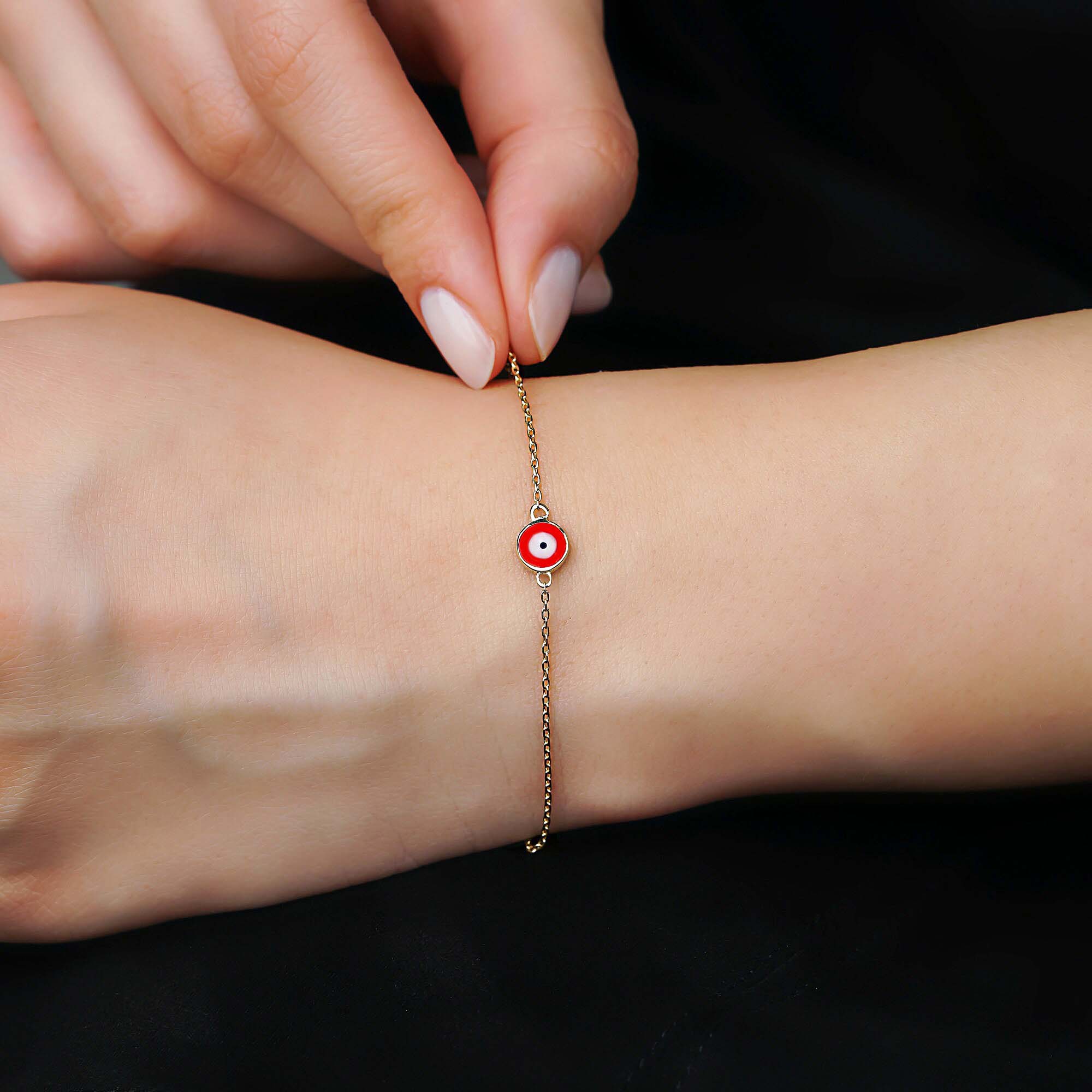 A 14k yellow gold cherry colored evil eye bracelet shown on a wrist.
