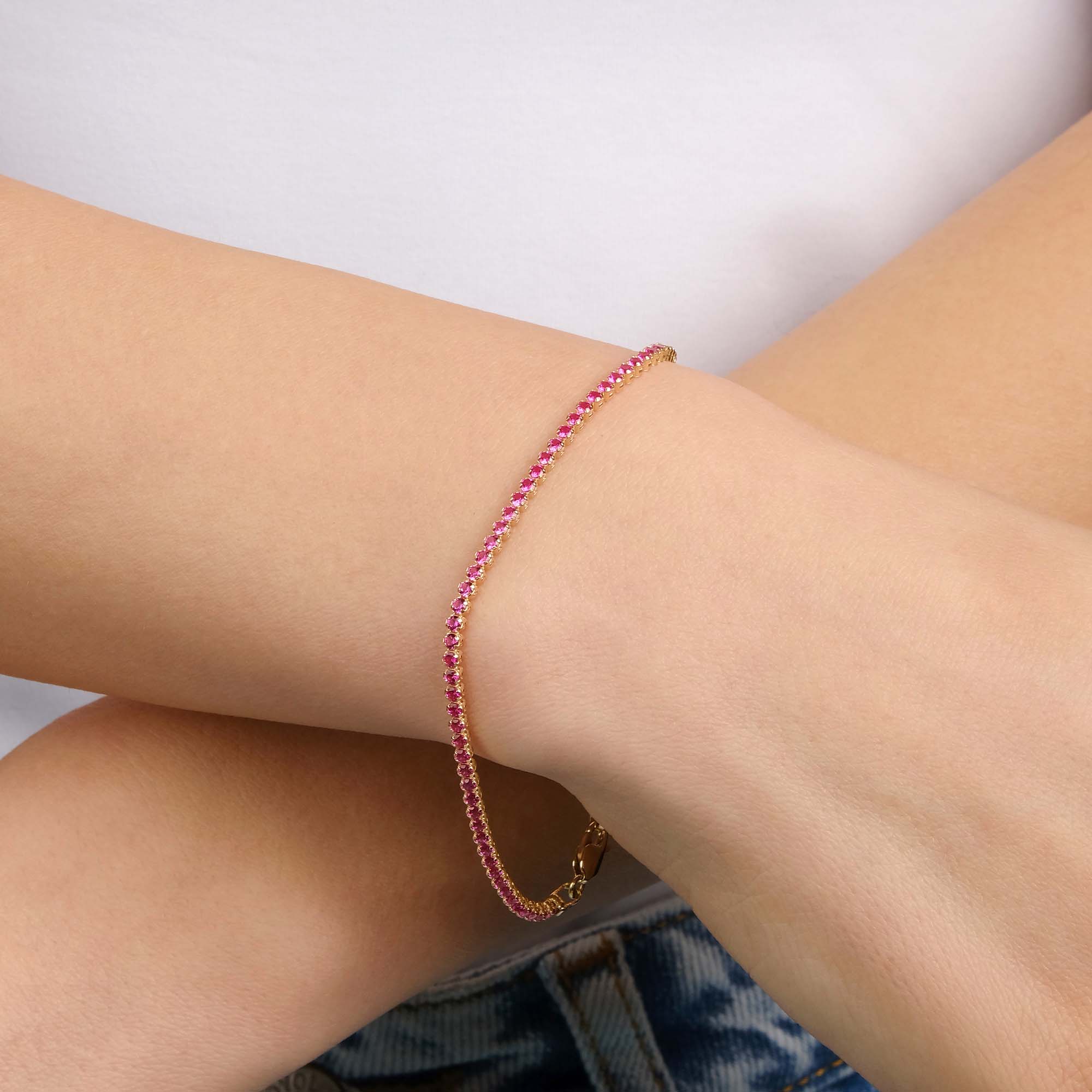 A created ruby tennis bracelet in 14K yellow gold with a width of 2.1 mm, featuring a series of red gemstones.