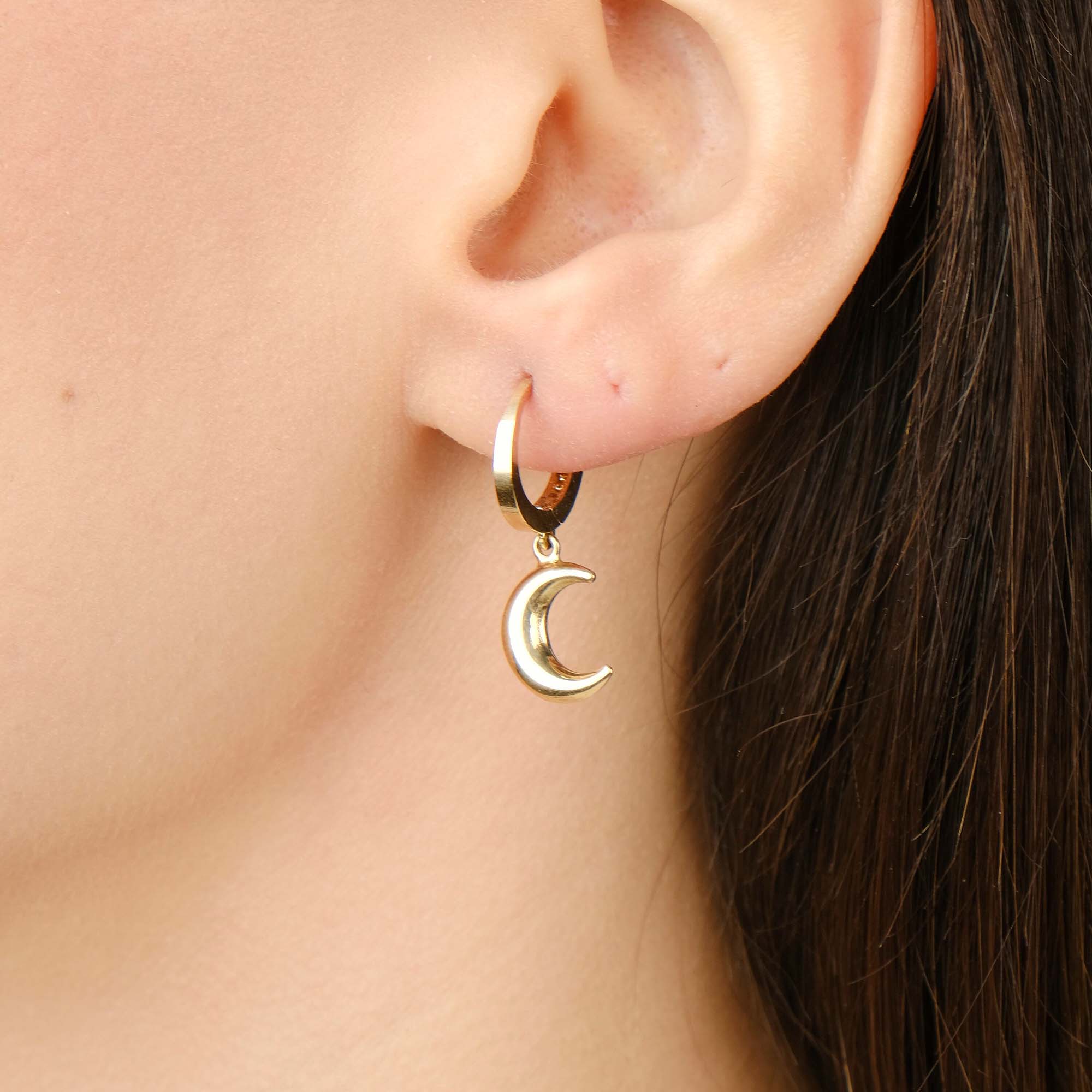 Gold hoop earring with a moon charm worn by a person