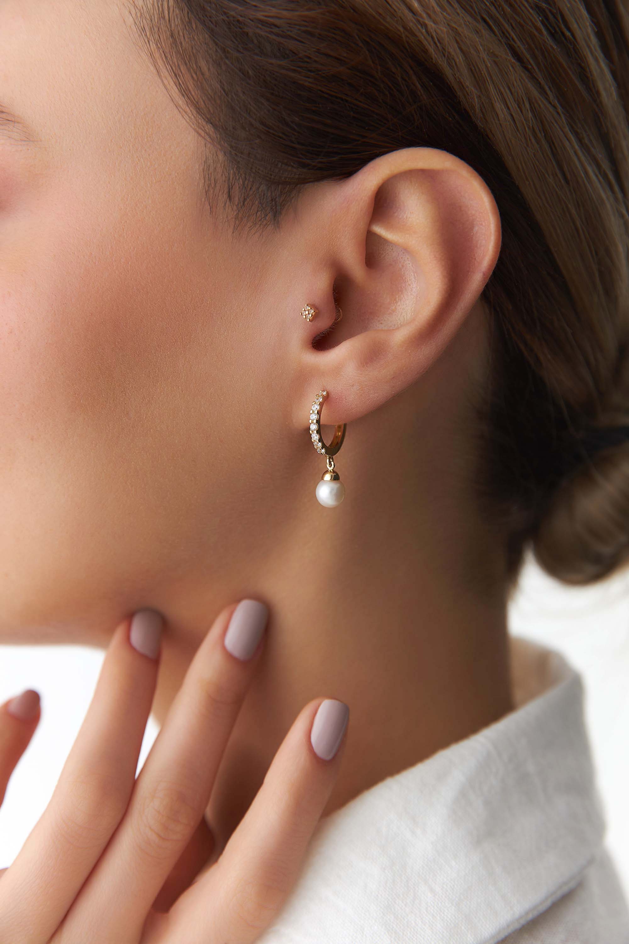 Close-up of a person wearing a gold hoop earring with a pearl drop on a neutral background