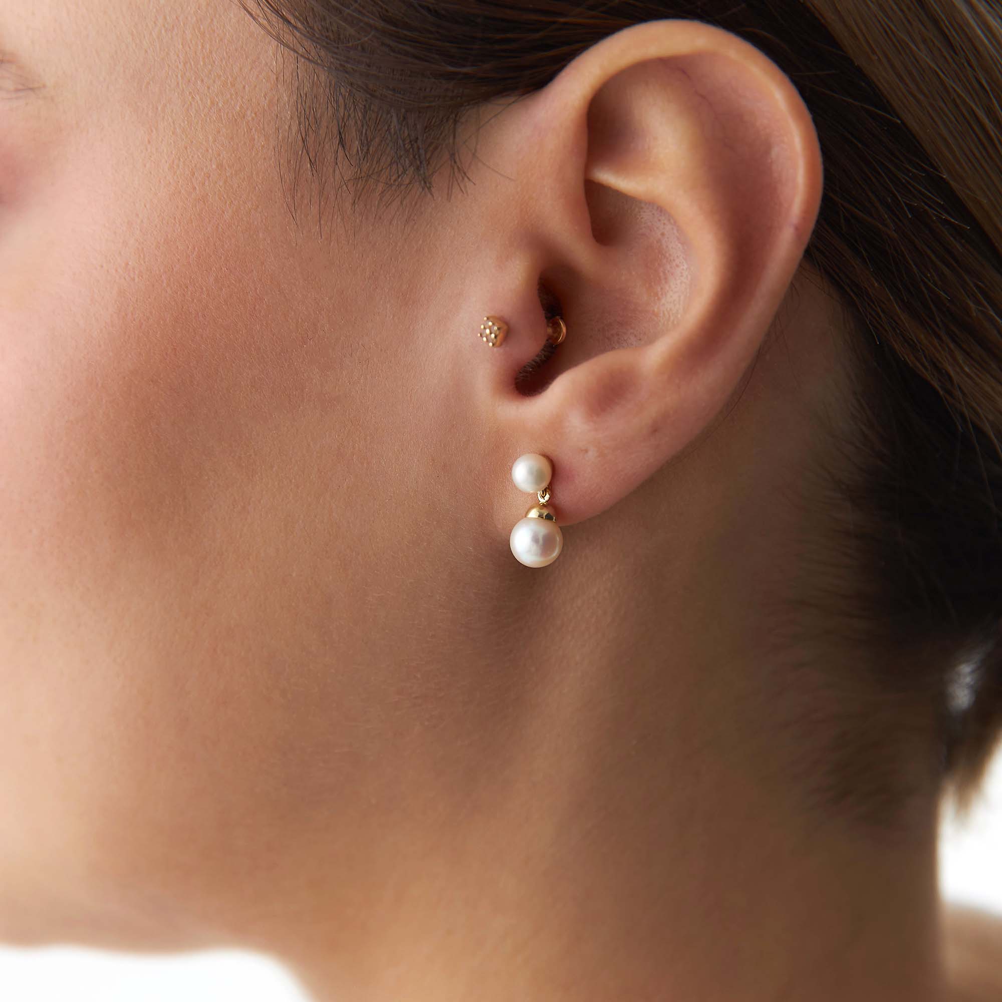 Close-up of an ear wearing gold and pearl earrings.