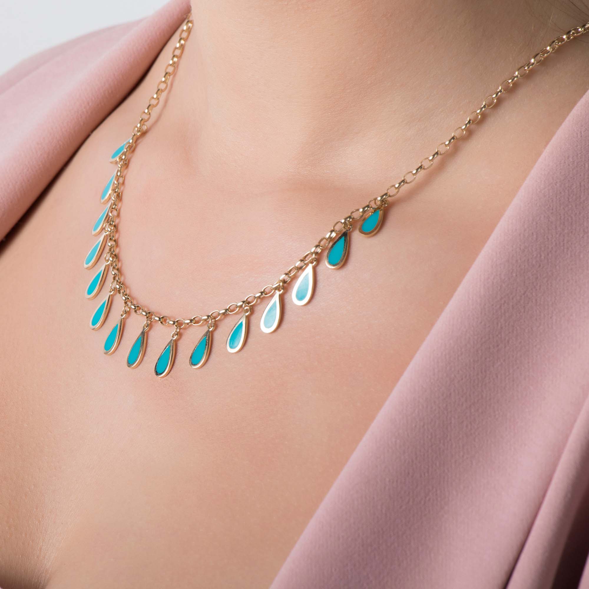 Gold necklace with blue raindrop pendants on a person wearing a pink top.