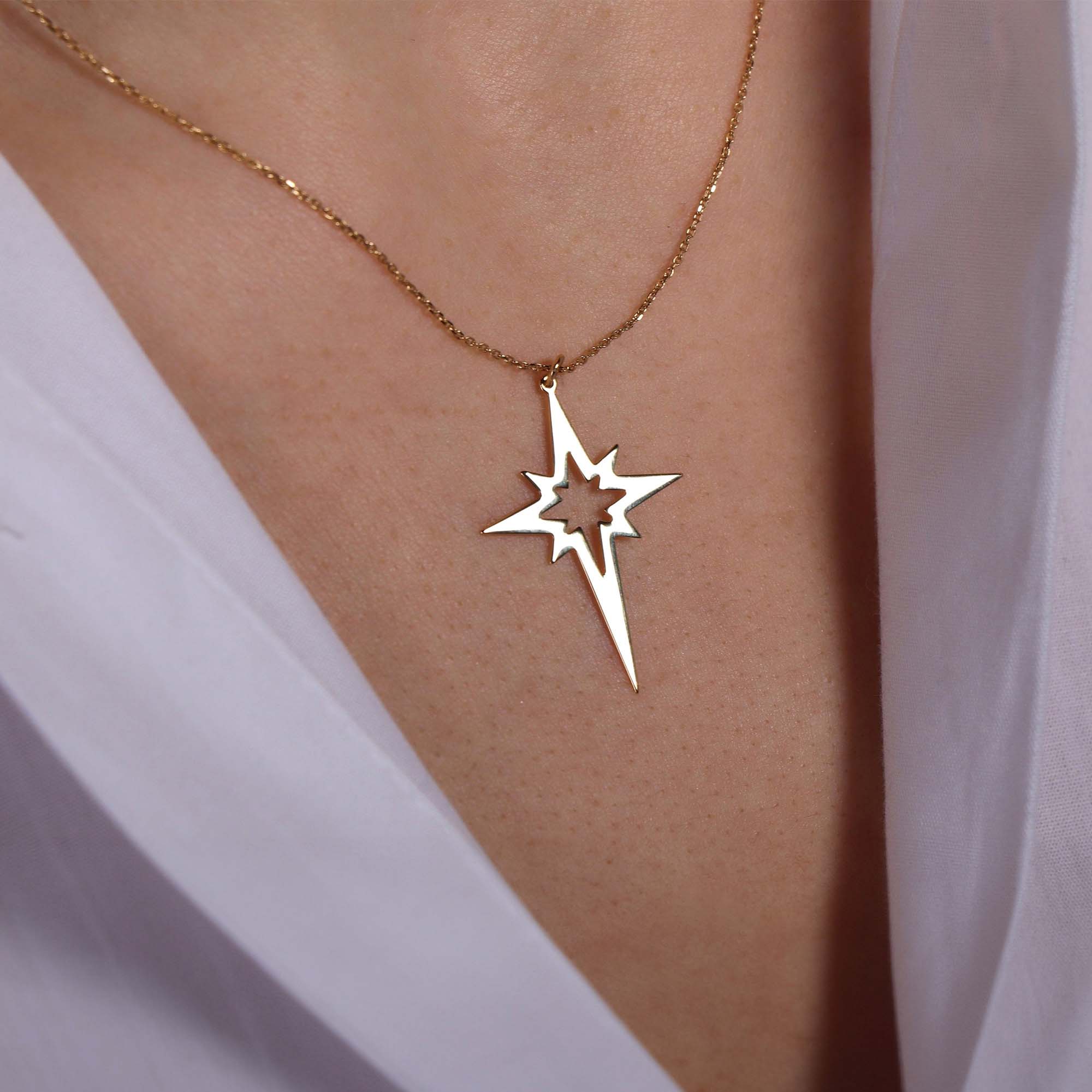 A 14k yellow gold elongated north star-shaped pendant necklace on a person wearing a white top