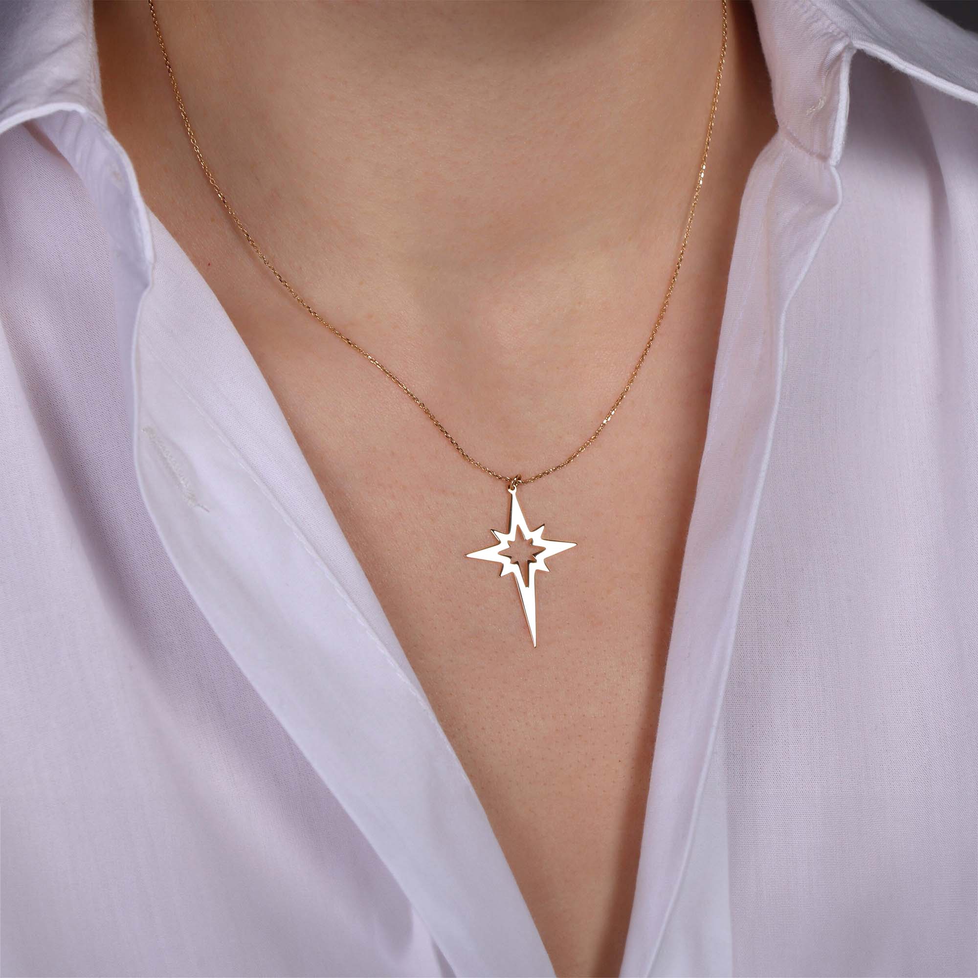 A 14k yellow gold elongated north star-shaped pendant necklace on a person wearing a white top