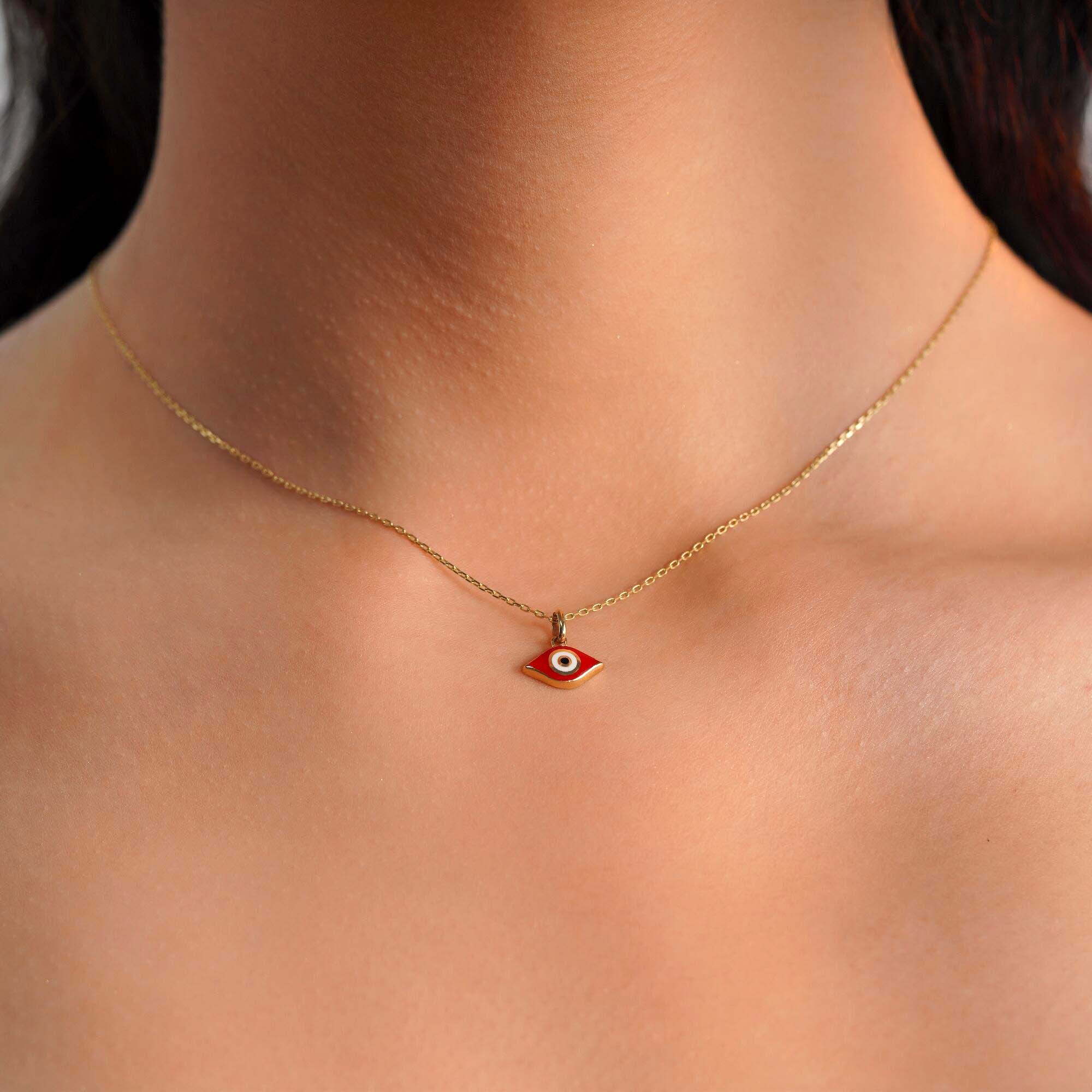 A model wearing an elongated red evil eye pendant on a thin gold chain.