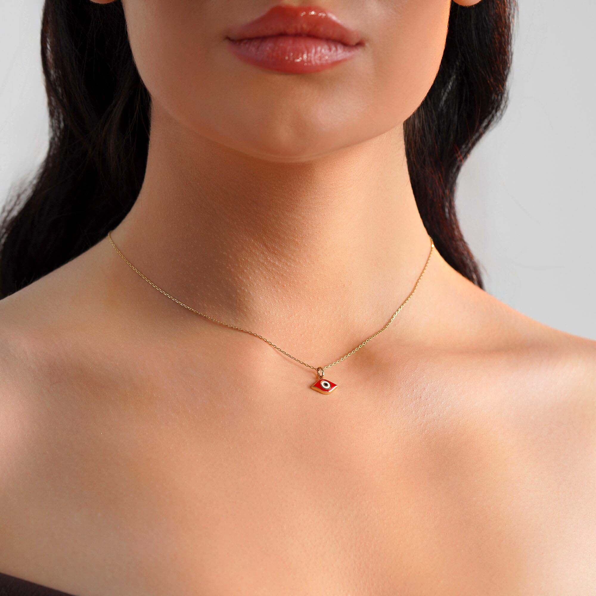 A model wearing an elongated red evil eye pendant on a thin gold chain.
