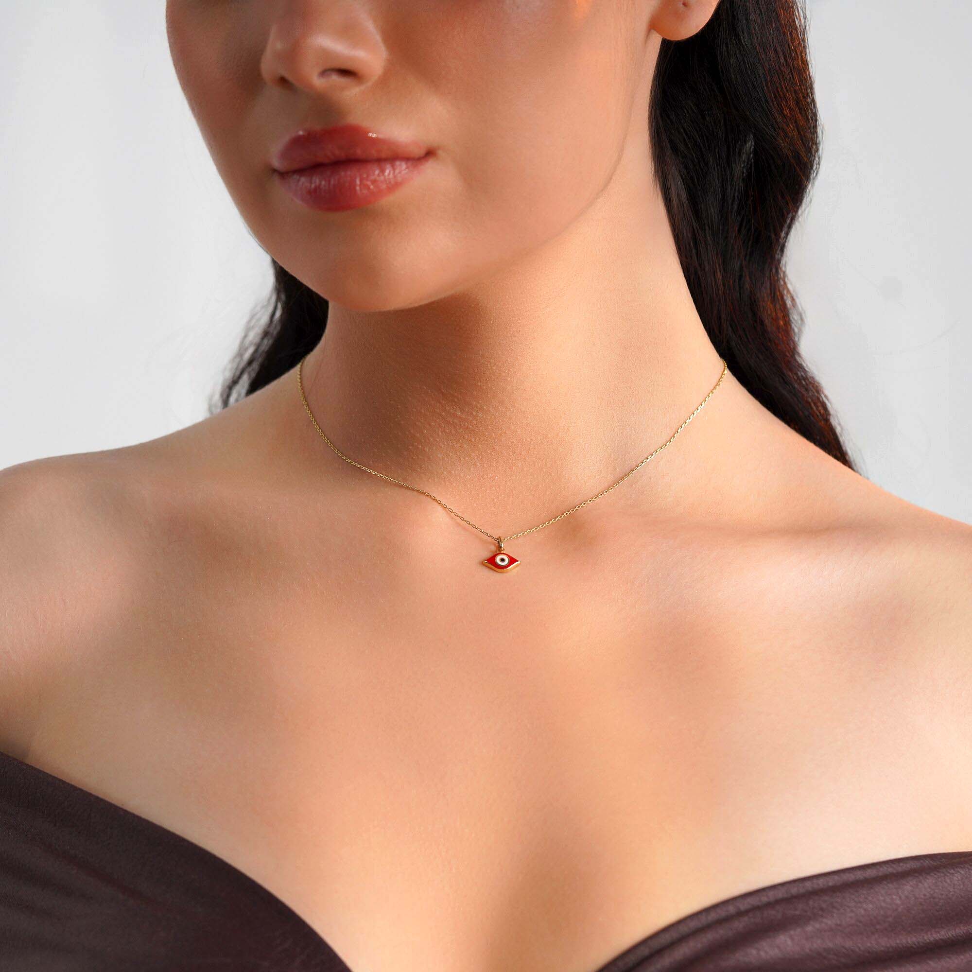 A model wearing an elongated red evil eye pendant on a thin gold chain.
