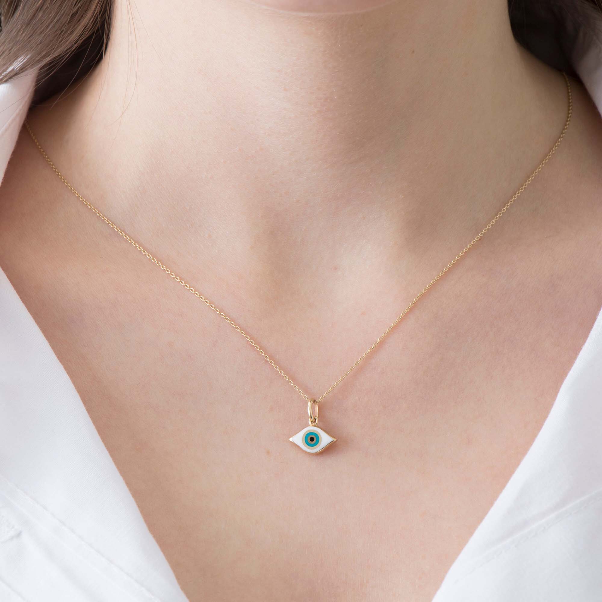 A 14k yellow gold necklace with an eye-shaped pendant on a person wearing a white top.