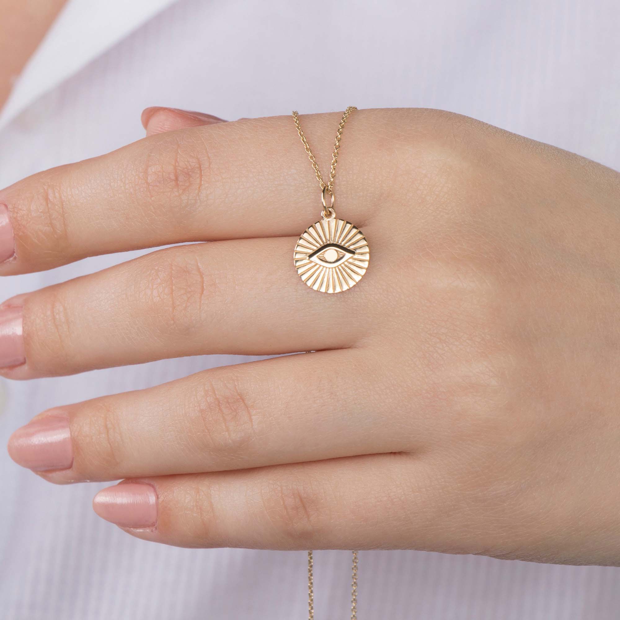 A model holding a 14k yellow gold evil eye coin pendant on a thin gold chain.