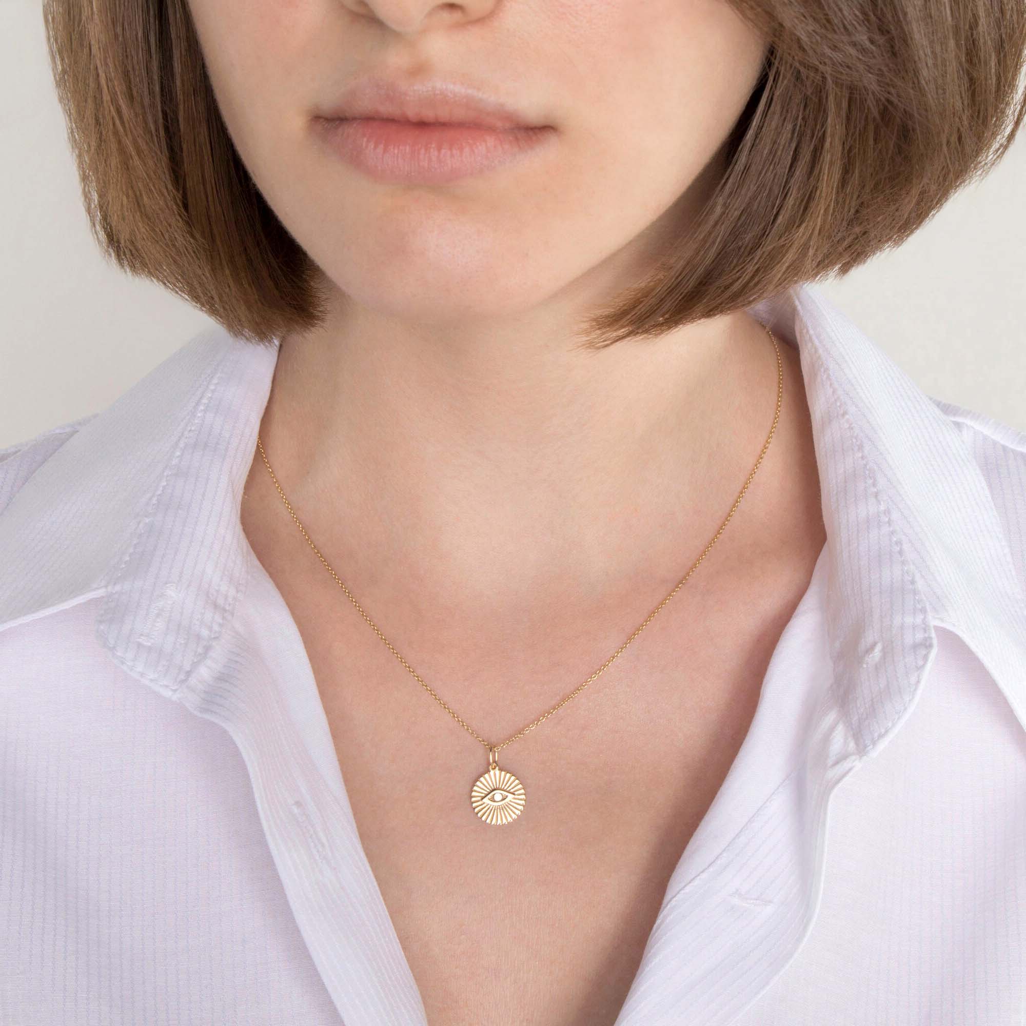 A model wearing a 14k yellow gold evil eye coin pendant on a thin gold chain.