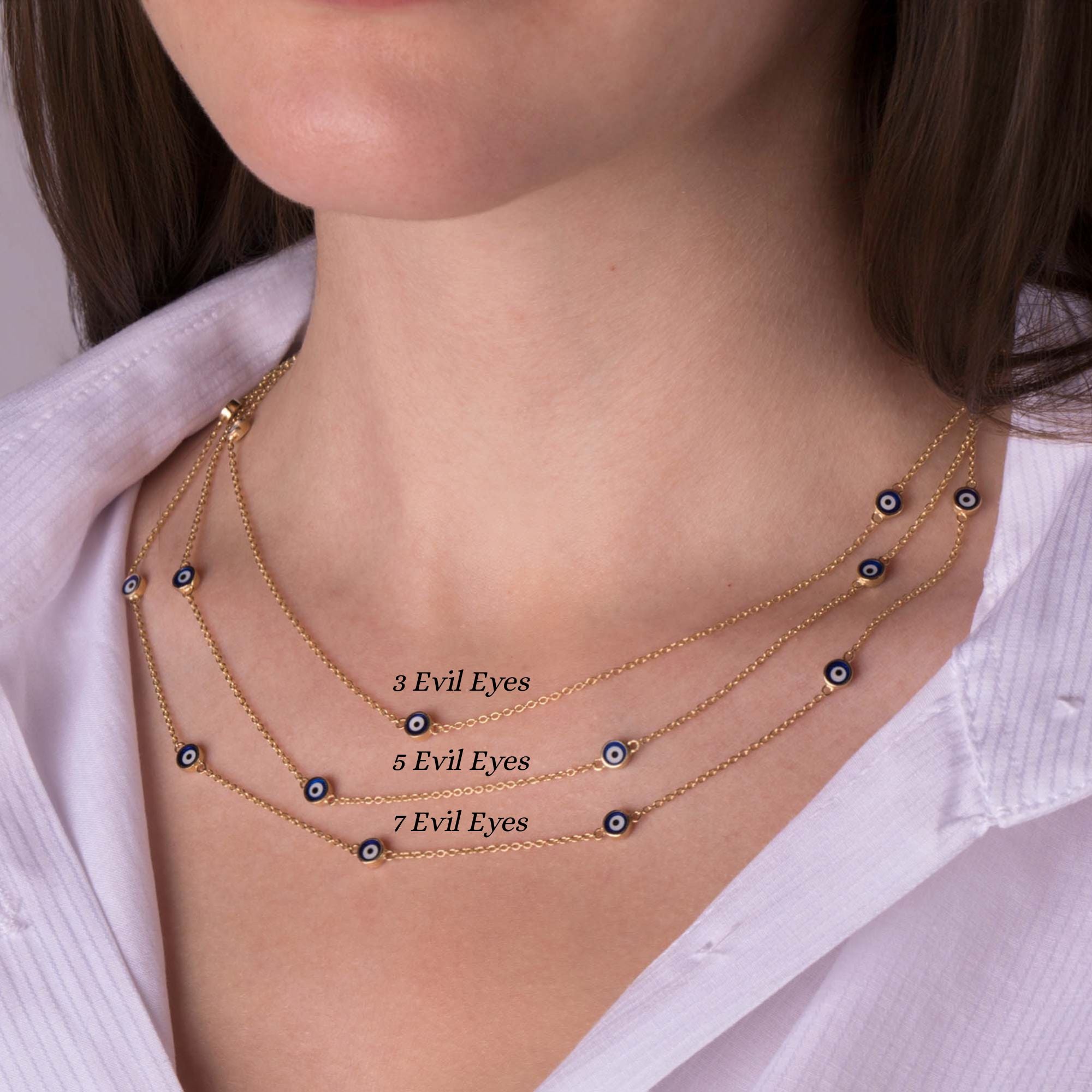 A model wearing three evil eye station necklaces. Top necklace has 3 evil eyes, the center necklace has 5 evil eyes, the bottom necklace has 7 evil eyes.