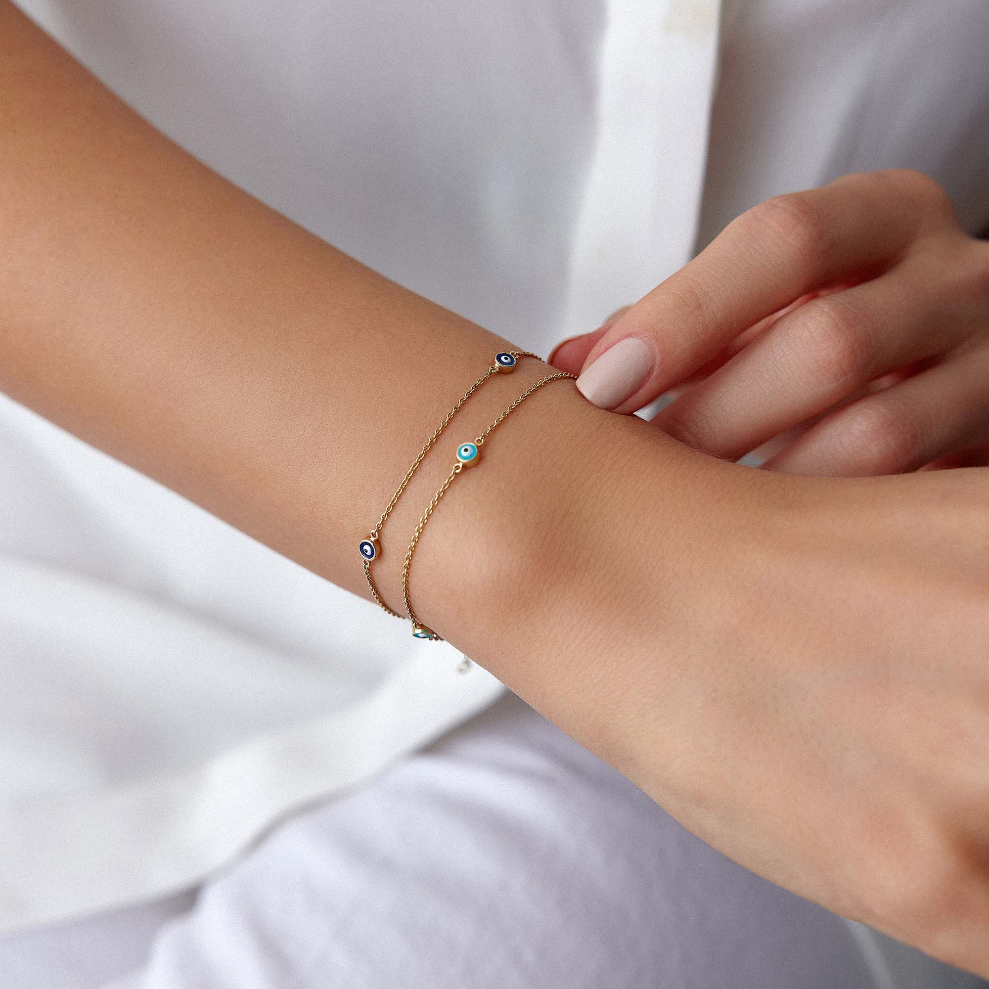 Person wearing two delicate bracelet with small evil eyes on a plain background