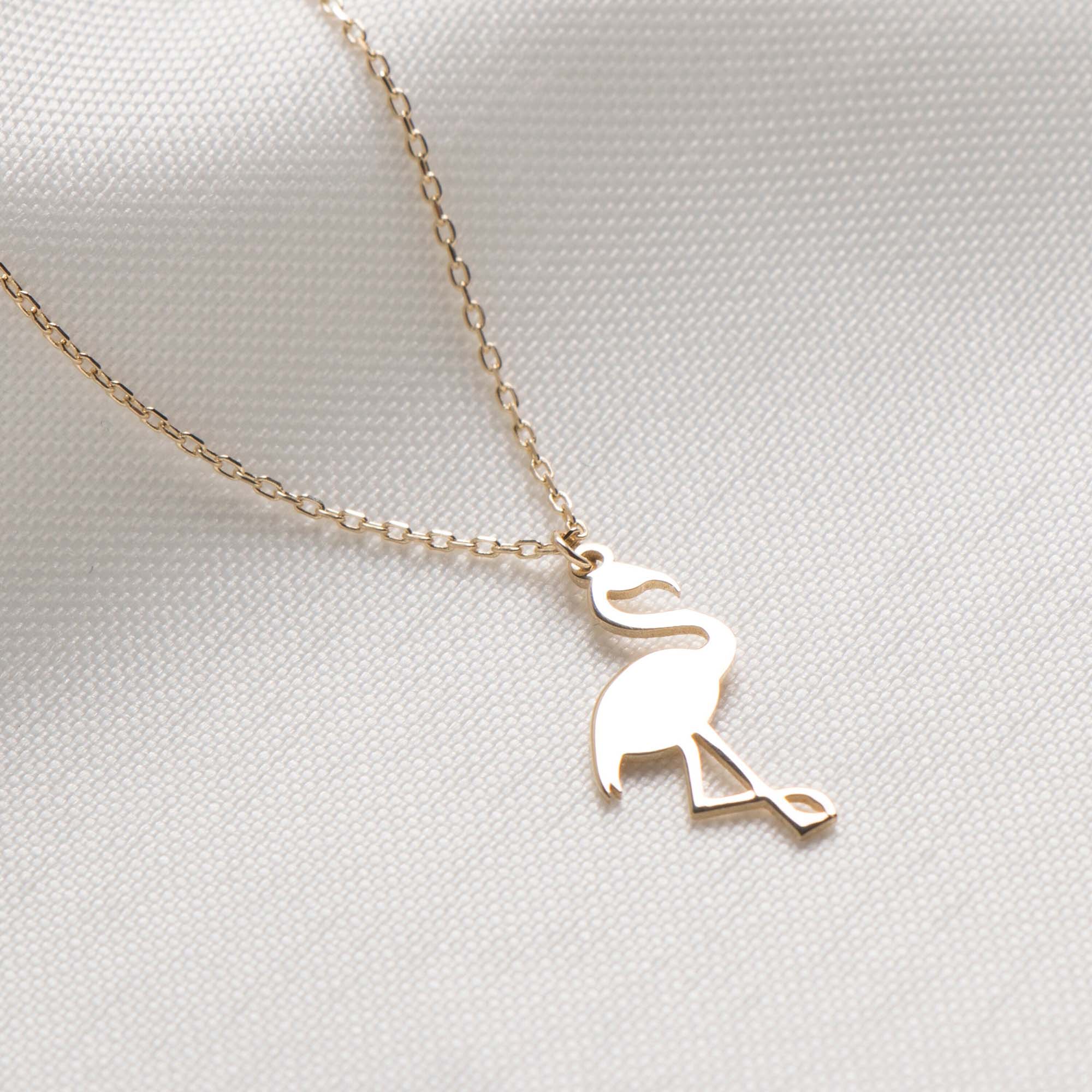 Gold flamingo pendant necklace on a light gray background