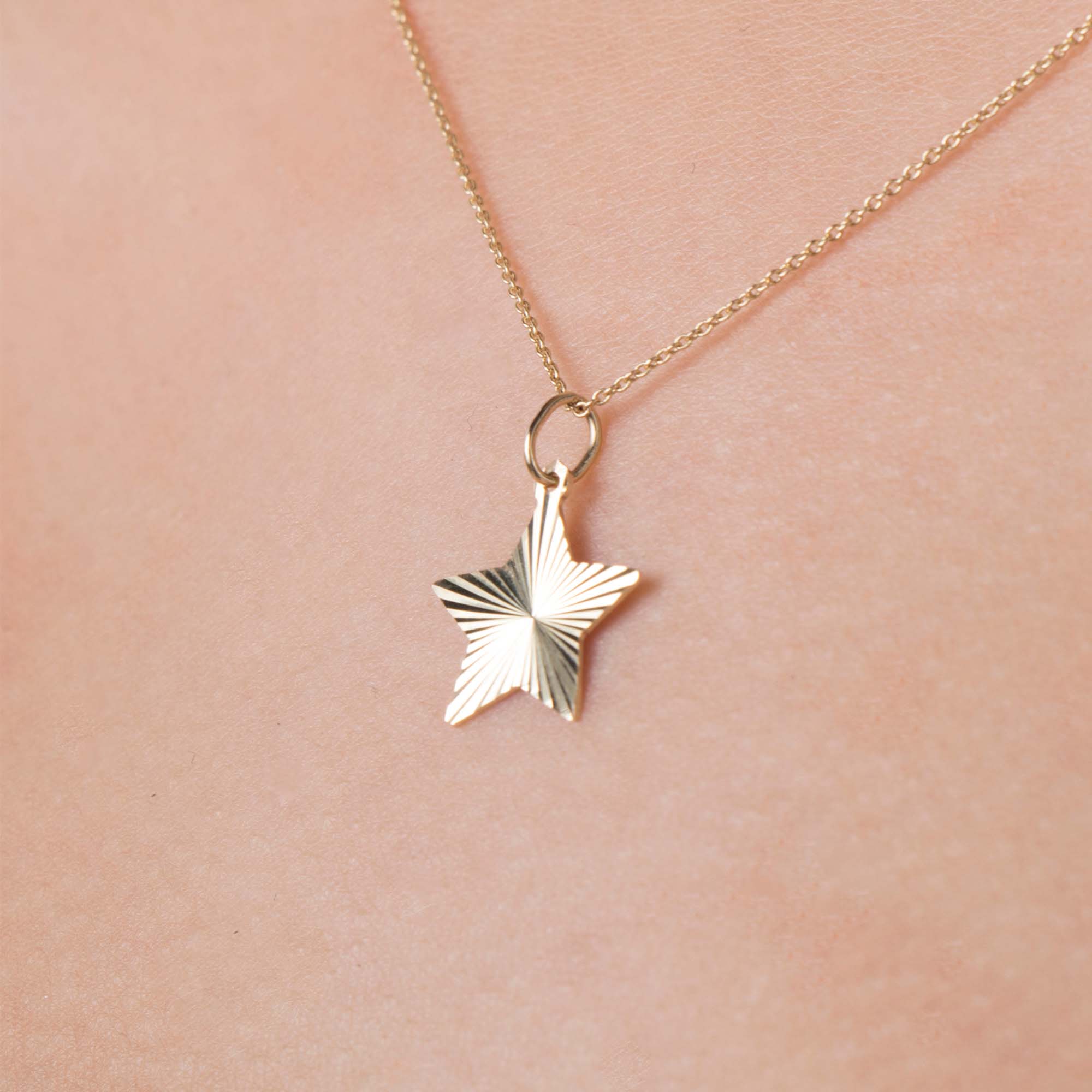 14k yellow gold star-shaped pendant necklace on a person wearing a pink garment.