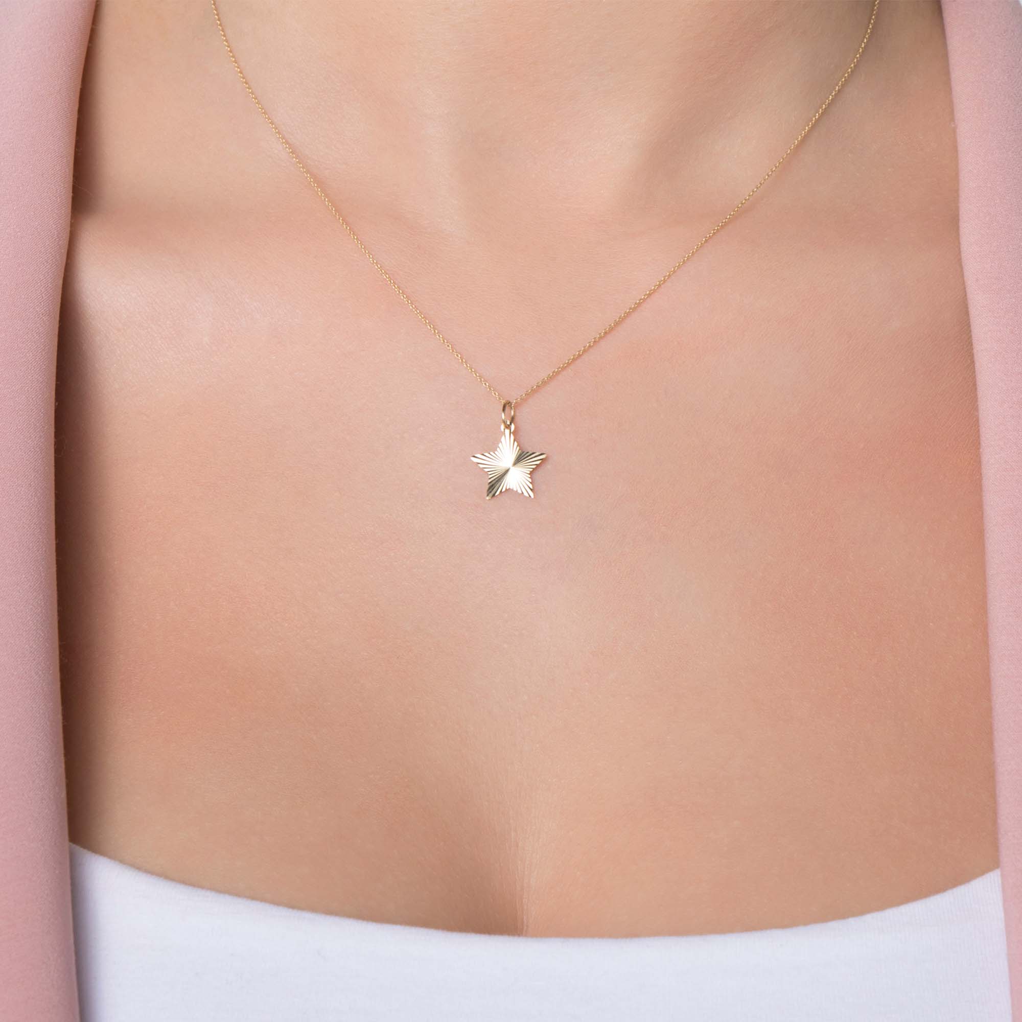14k yellow gold star-shaped pendant necklace on a person wearing a pink garment.