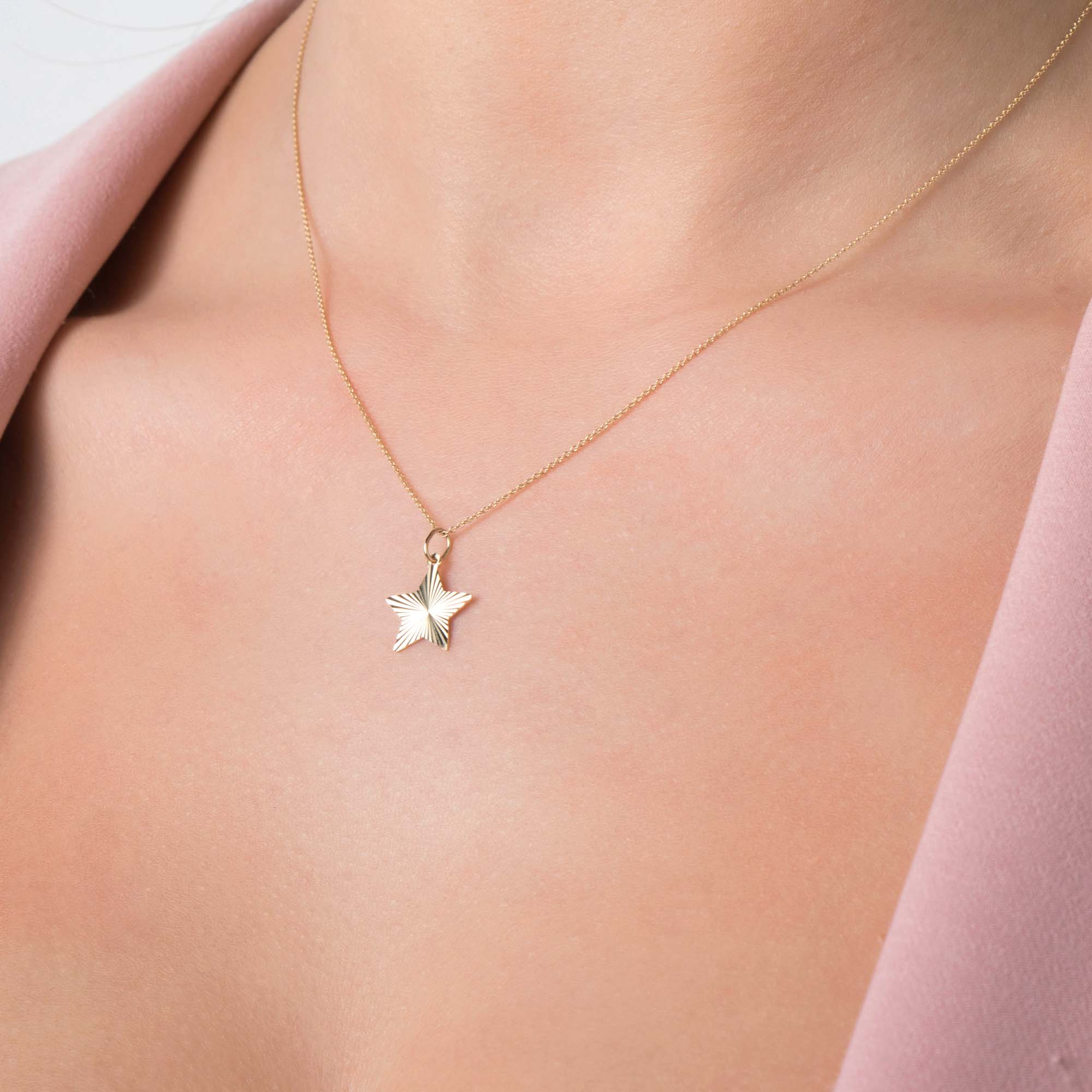 14k yellow gold star-shaped pendant necklace on a person wearing a pink garment.