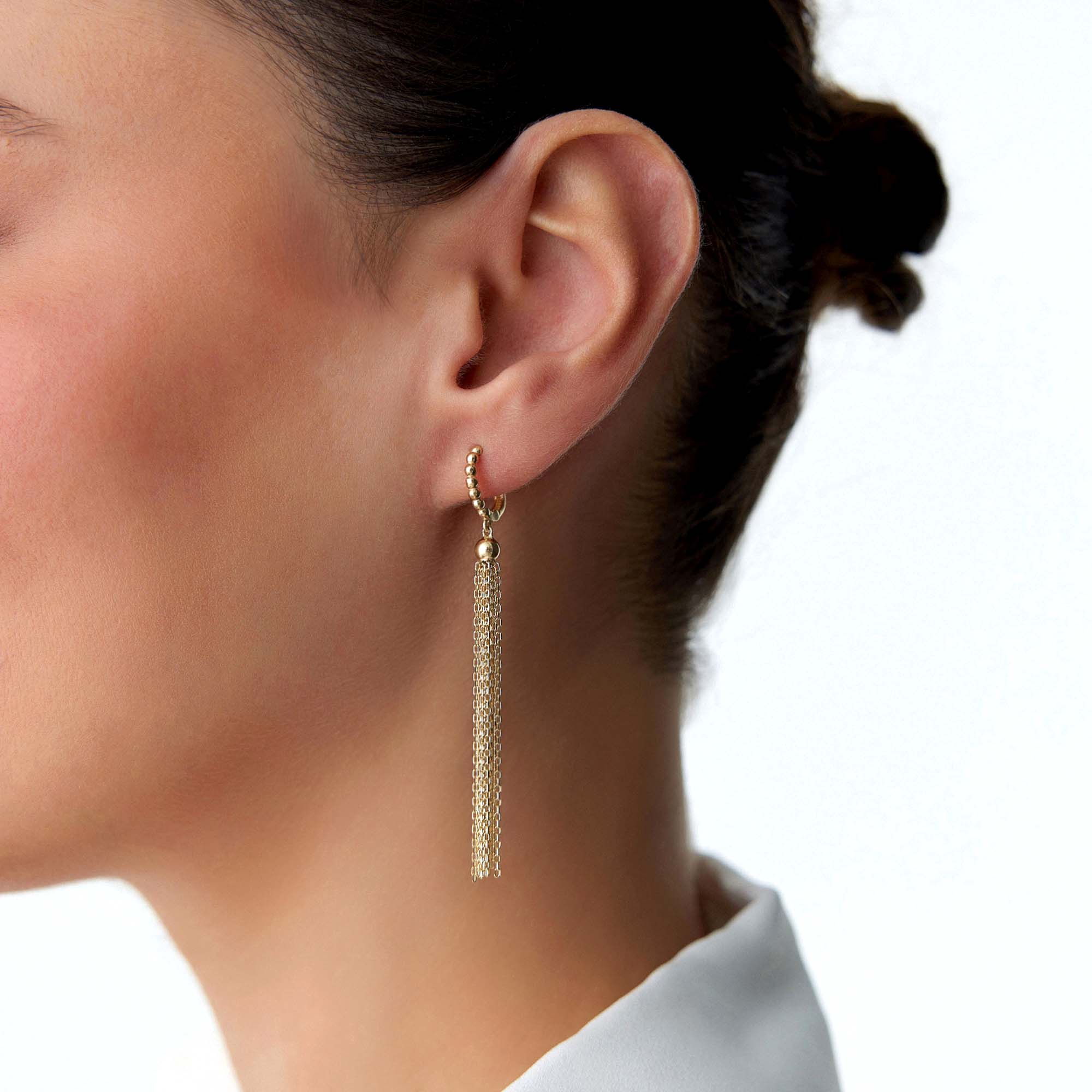 Gold hoop earring with chain tassel worn by a person on a white background