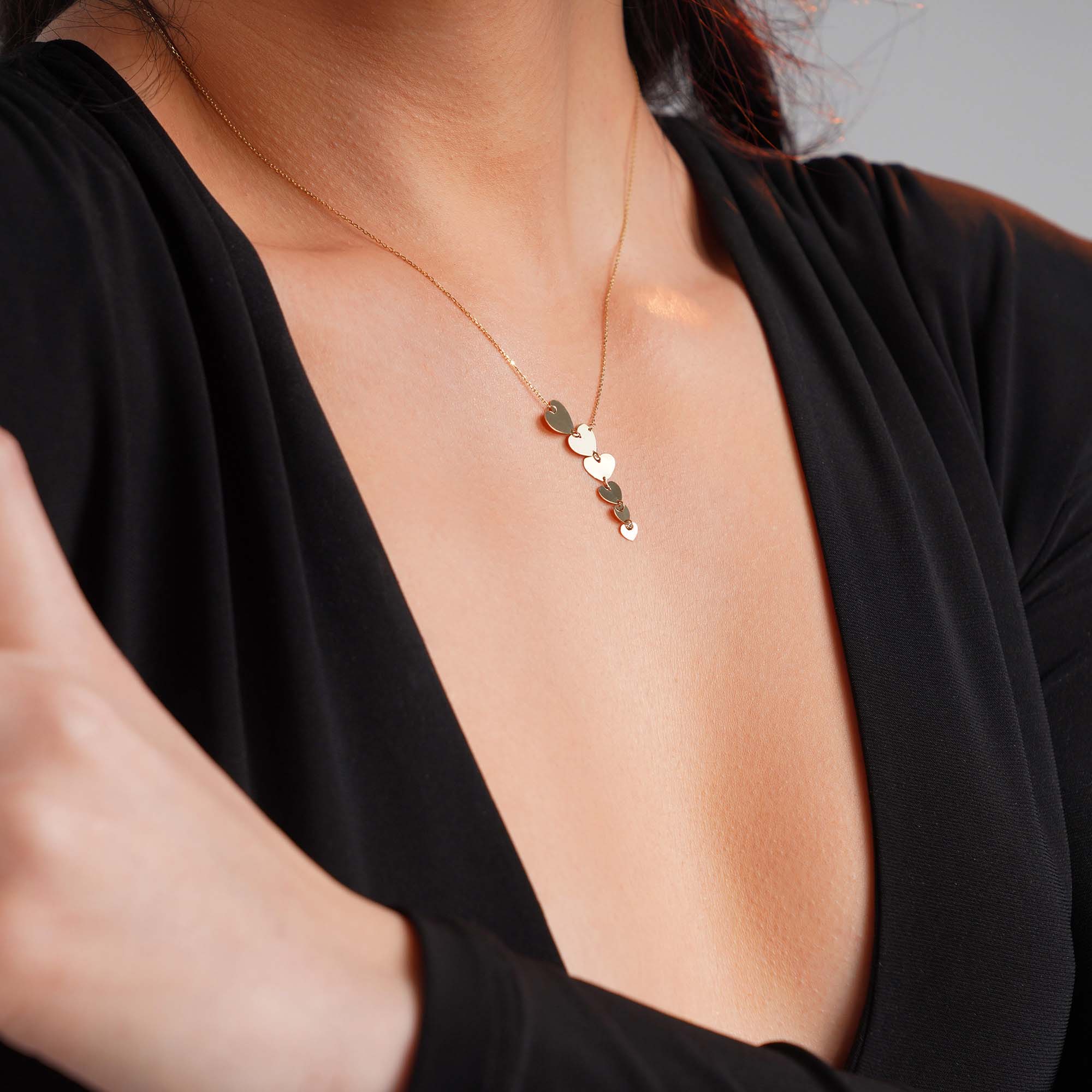 A graduated heart lariat necklace worn by a model shown upclose.