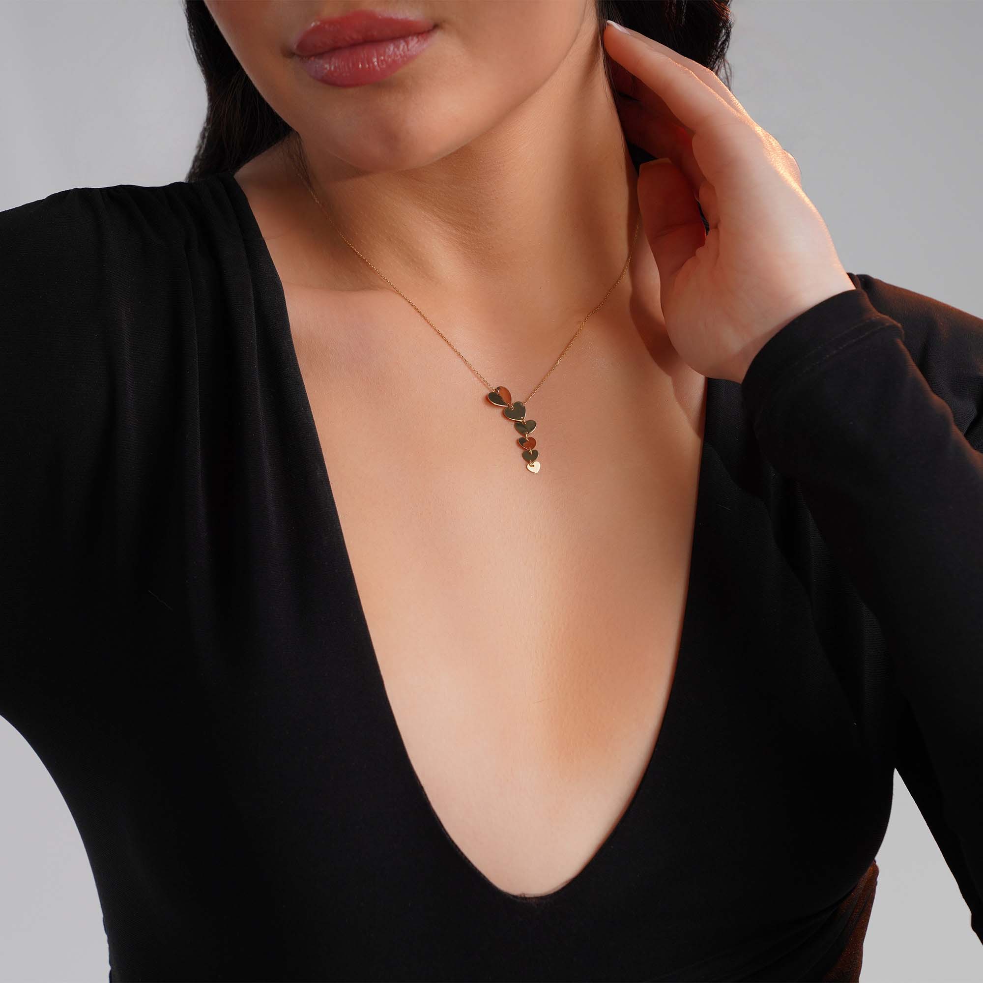A graduated heart lariat necklace worn by a model shown upclose.