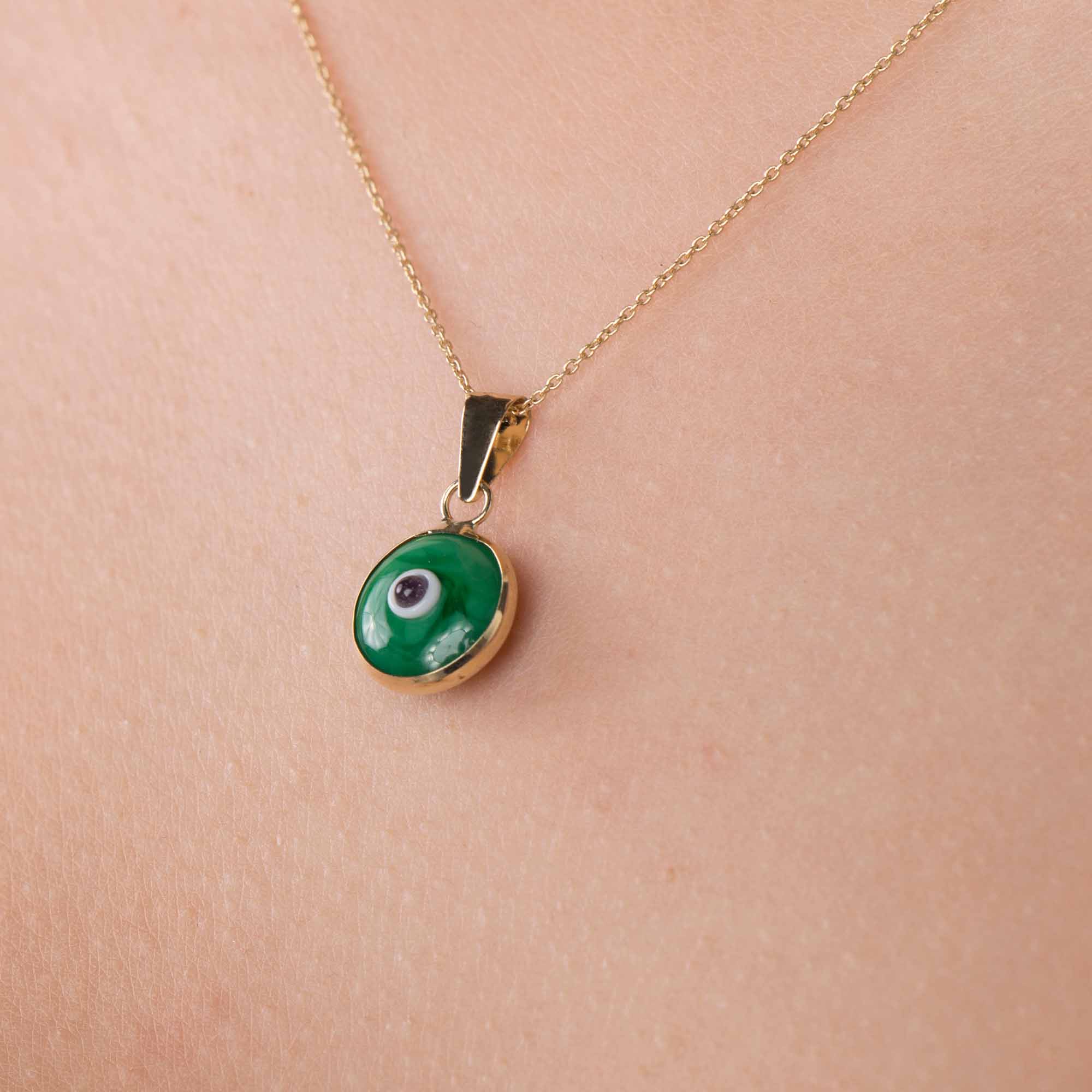 An up-close image of an opaque green evil eye pendant worn on a golden chain