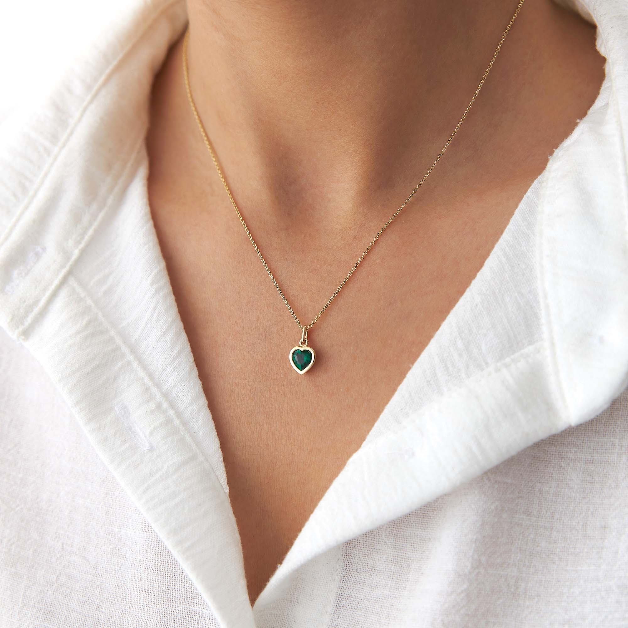 Gold necklace with a heart-shaped green pendant worn by a person in a white shirt.