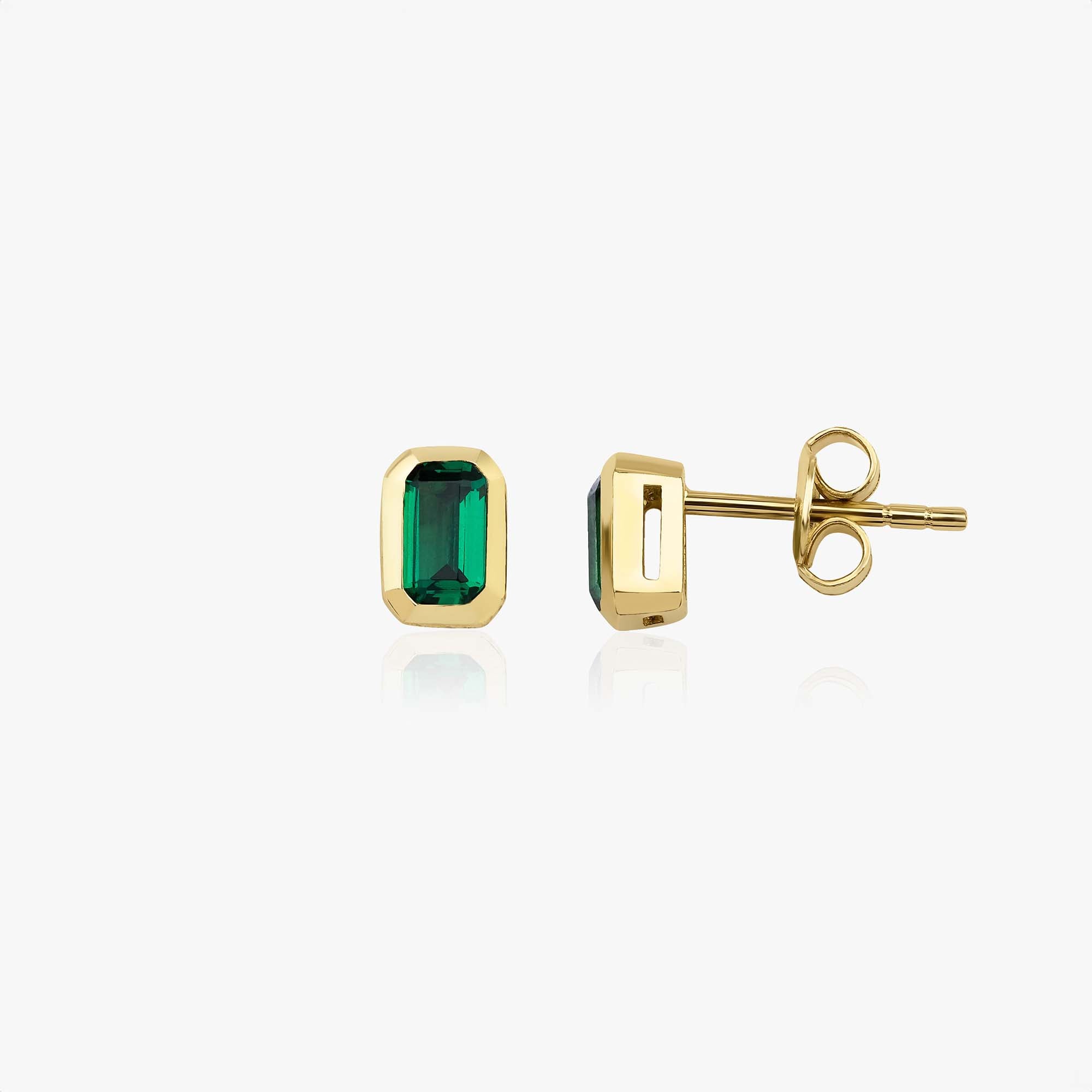 Gold earrings with green gemstones on a white background, one shown sideways