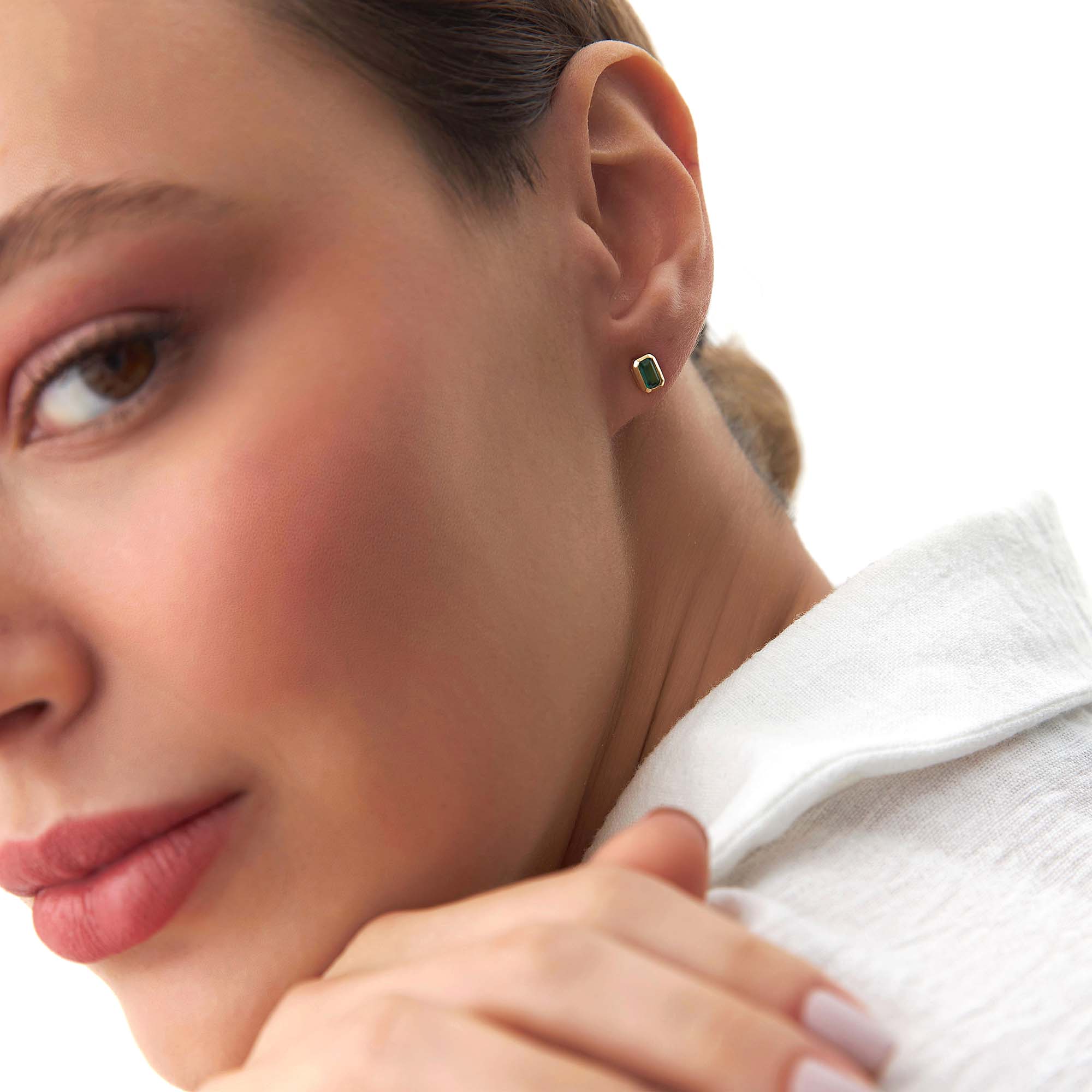 Close-up of a woman wearing a green gemstone earring on a white background