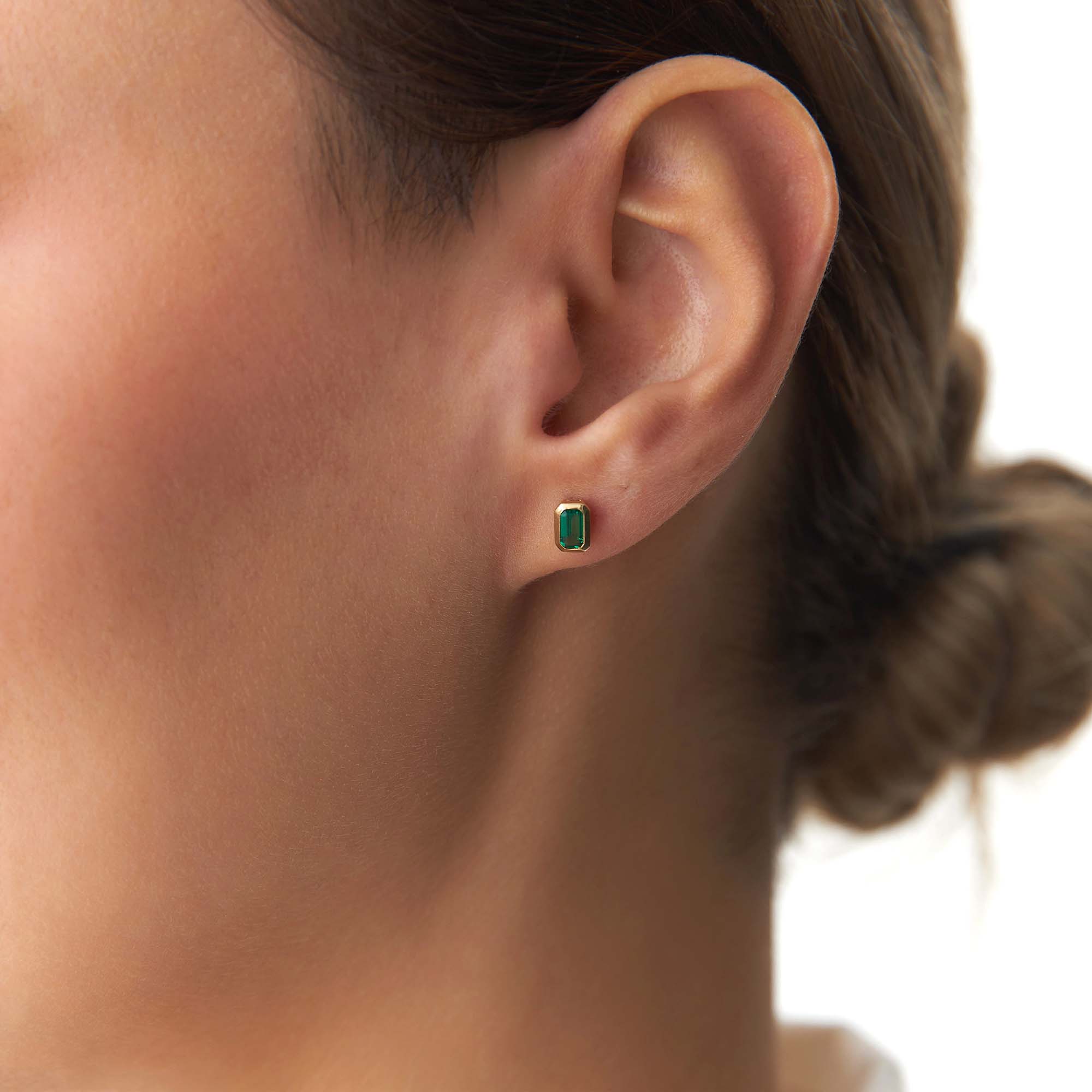 Close-up of an ear wearing a green emerald stud earring with blurred background