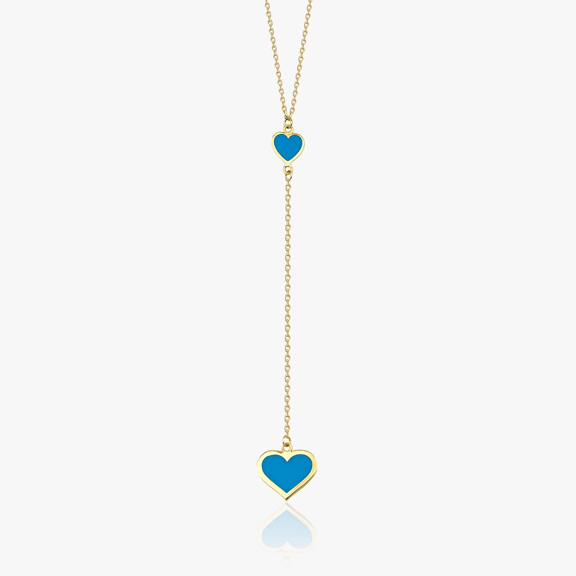 A gold lariat necklace with two heart charms, the first small and solid gold, the second larger with turquoise color enamel, suspended from a gold chain.