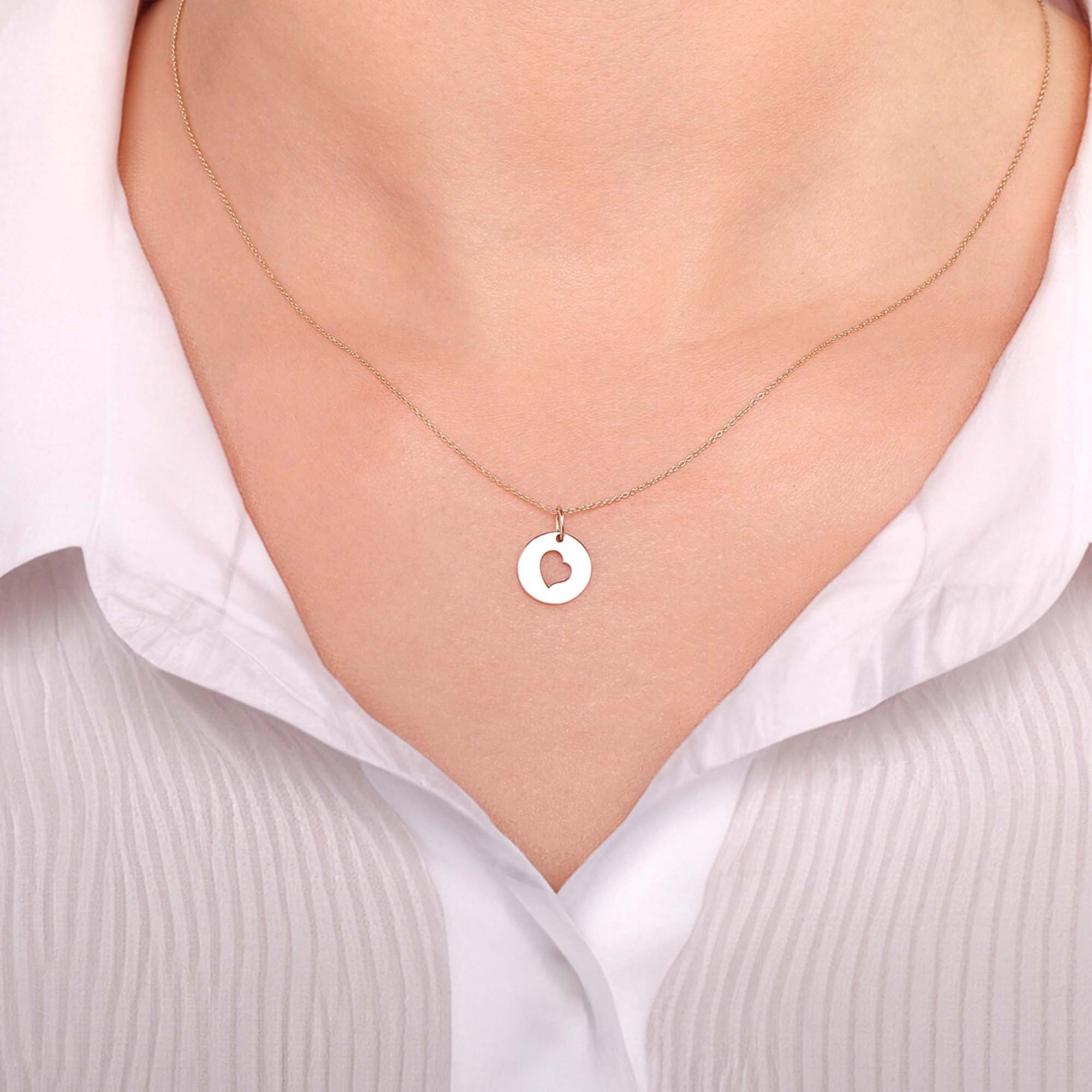 A 14k yellow gold necklace with a heart pendant worn by a model wearing a white shirt.