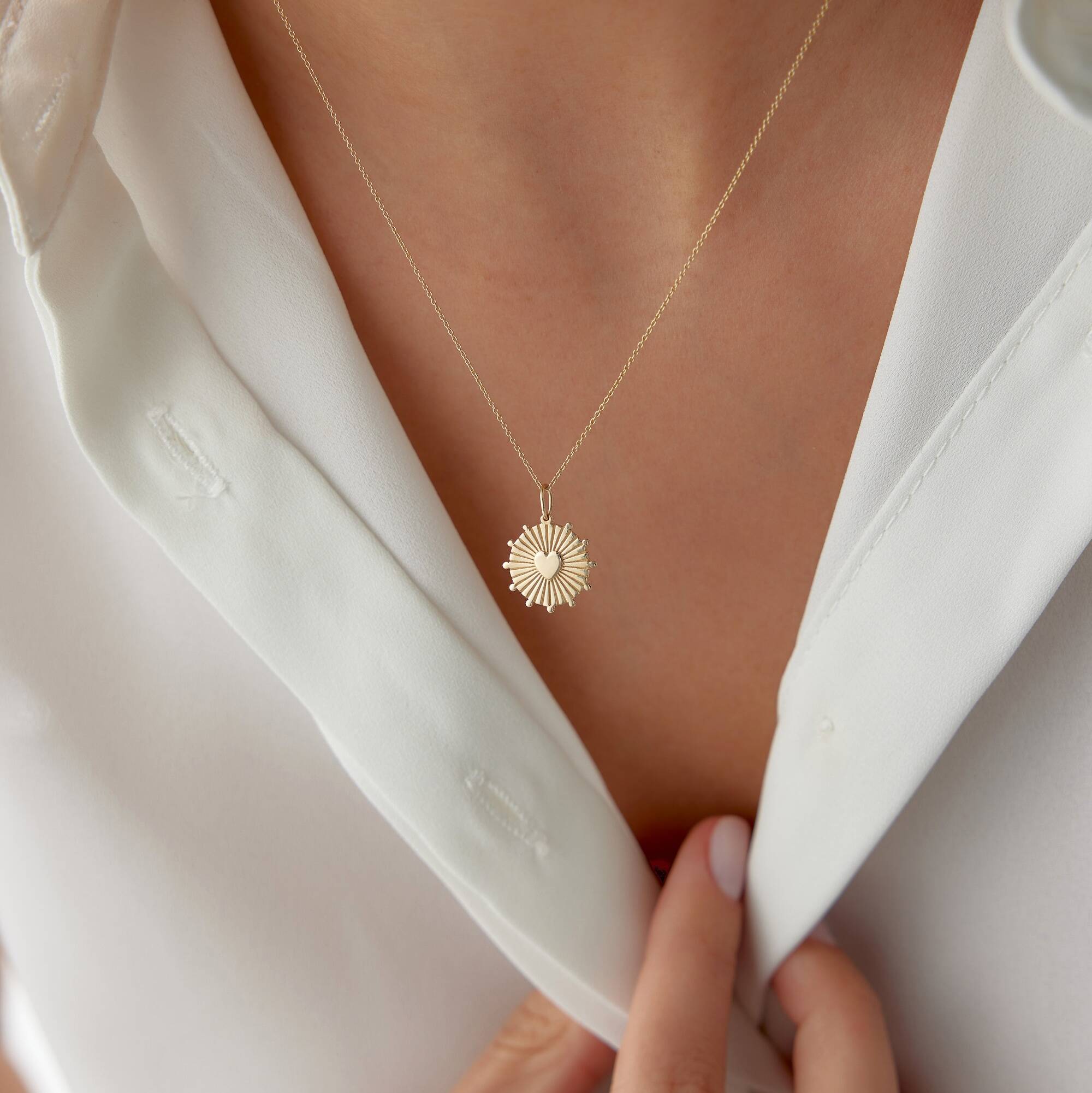A model wearing a 14k yellow gold heartburst coin pendant on a thin gold chain.