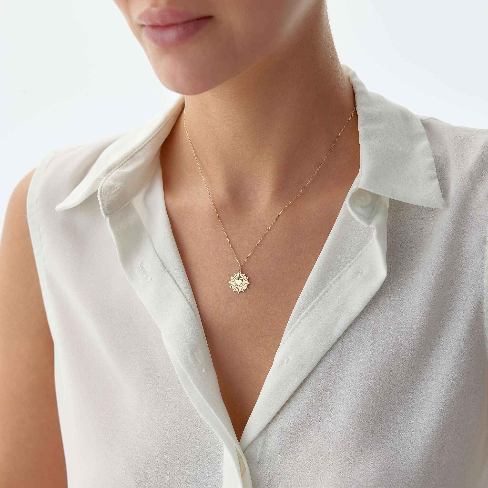 A model wearing a 14k yellow gold heartburst coin pendant on a thin gold chain.