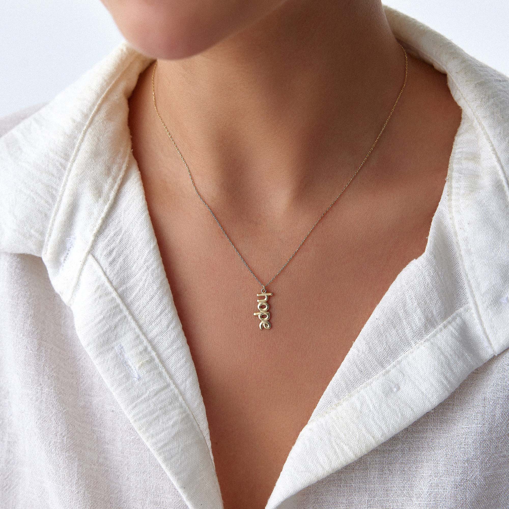 Gold 'hope' necklace on a person wearing a white shirt.