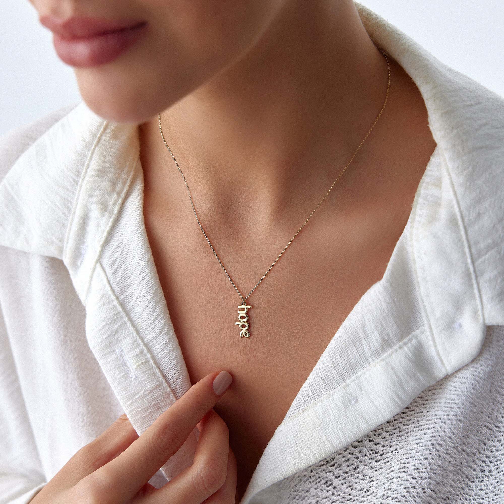 Gold 'hope' necklace on a person wearing a white shirt.